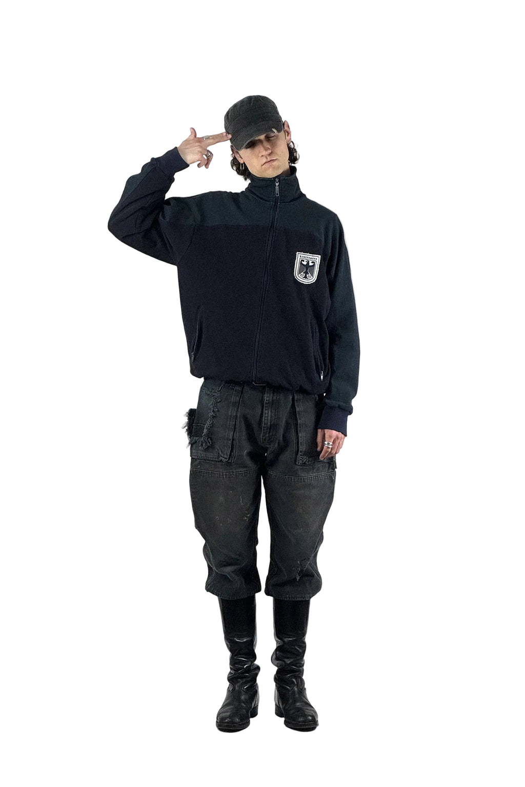 Dark-Workwear-Outfit mit einer dunkelblauen Vintage Bundeswehr Trainingsjacke inklusive Bundesadler-Wappen, thrashed Dickies Double Knee Pants in Schwarz und hohen schwarzen Lederstiefeln vor weißem Studiohintergrund.