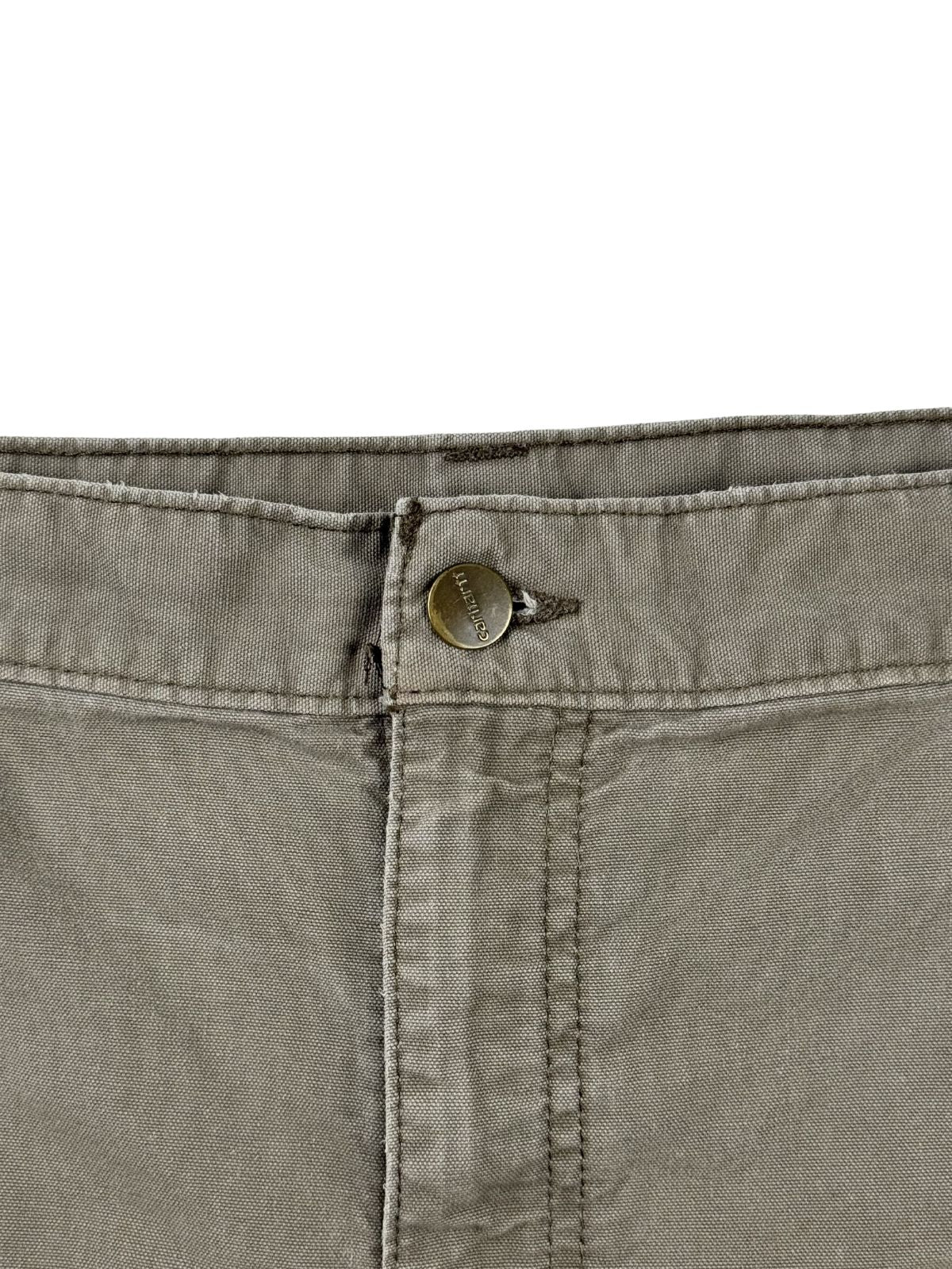 Makroaufnahme des Hosenbunds mit dem originalen, geprägten Carhartt Metallknopf über dem Reißverschluss.