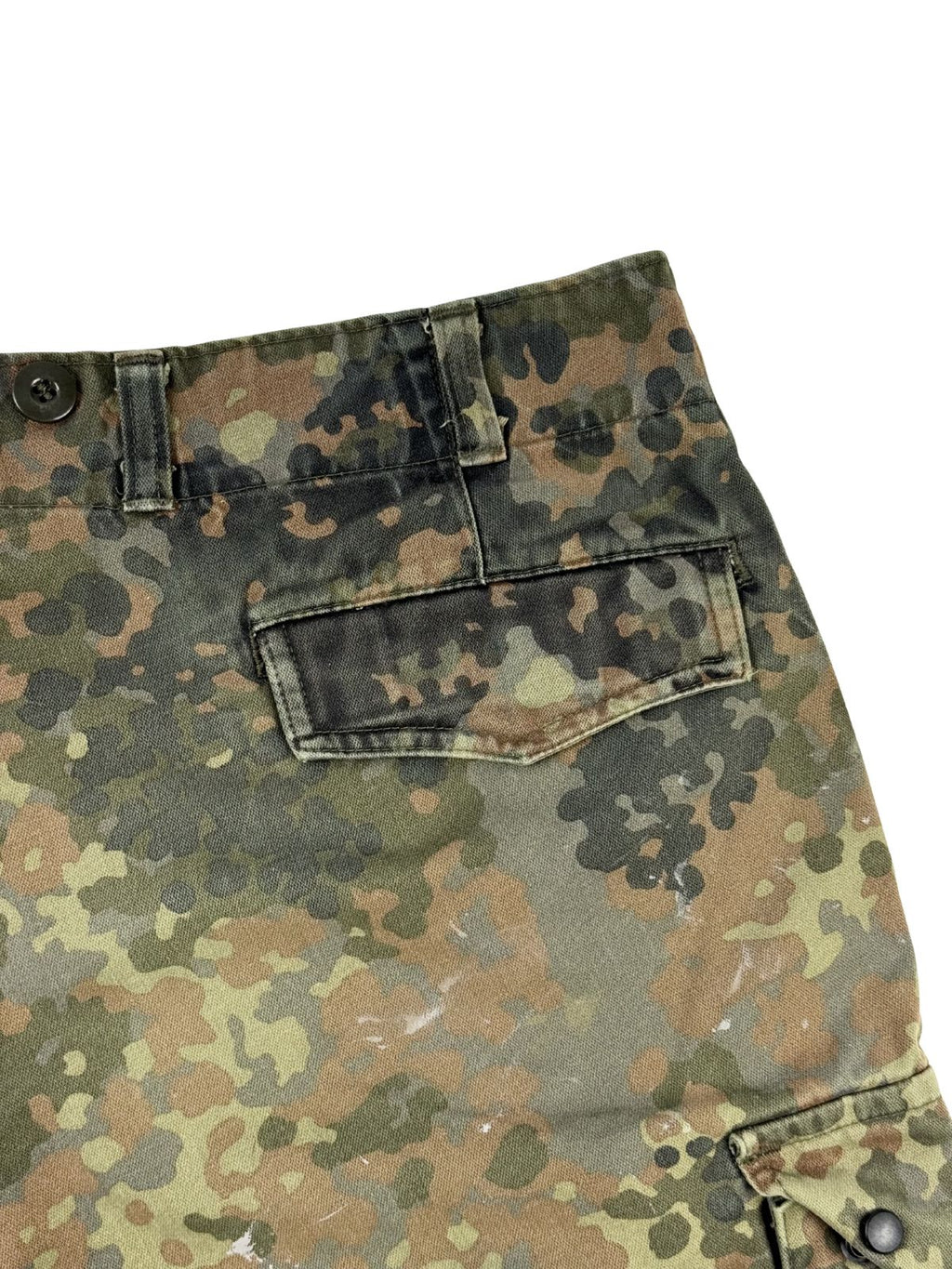Detailaufnahme der rechten Gesäßtasche mit verdeckter Knopfleiste unter einer Stoffklappe im Flecktarn-Muster.