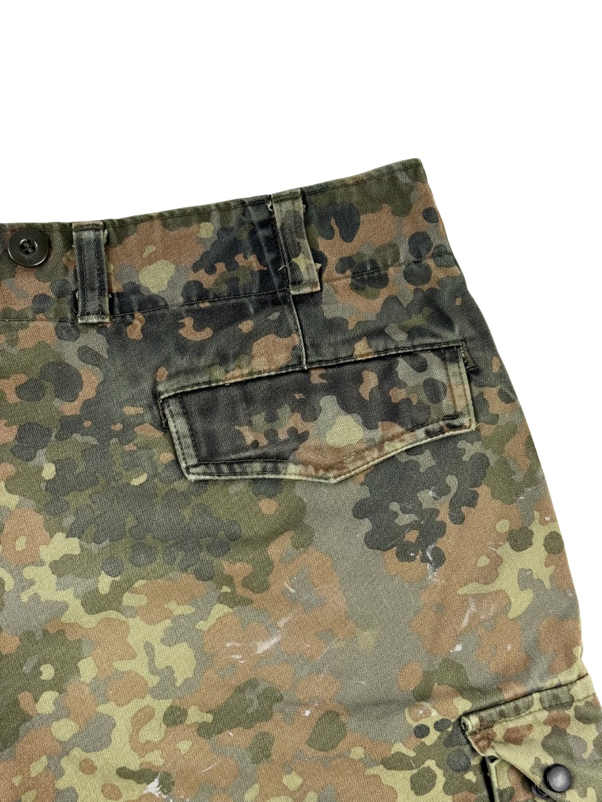 Detailaufnahme der rechten Gesäßtasche mit verdeckter Knopfleiste unter einer Stoffklappe im Flecktarn-Muster.