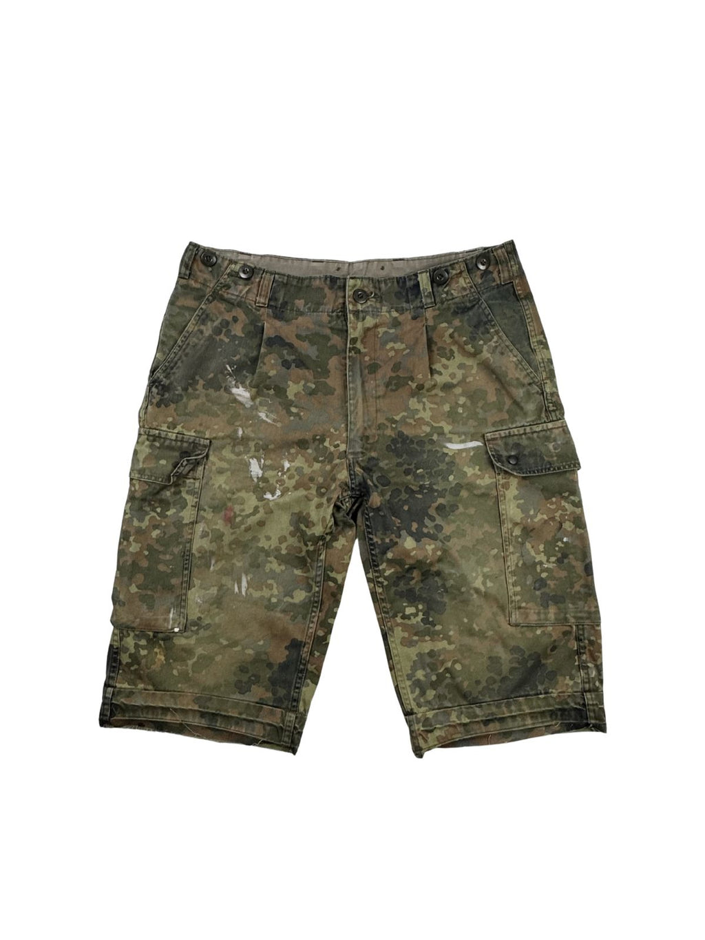 Komplettansicht der Vorderseite einer gebrauchten Bundeswehr Cargo-Shorts im klassischen Flecktarn-Camouflage. Die kurze Hose wurde individuell abgeschnitten (cut-off), zeigt authentische weiße Farbflecken im Distressed-Look und verfügt über zwei große Beintaschen. Flatlay auf weißem Hintergrund.