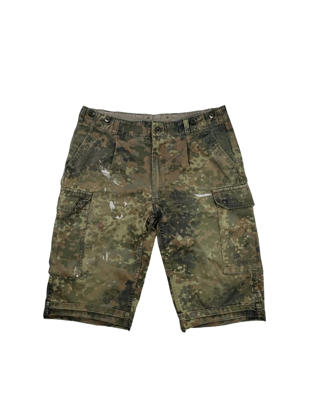 Komplettansicht der Vorderseite einer gebrauchten Bundeswehr Cargo-Shorts im klassischen Flecktarn-Camouflage. Die kurze Hose wurde individuell abgeschnitten (cut-off), zeigt authentische weiße Farbflecken im Distressed-Look und verfügt über zwei große Beintaschen. Flatlay auf weißem Hintergrund.