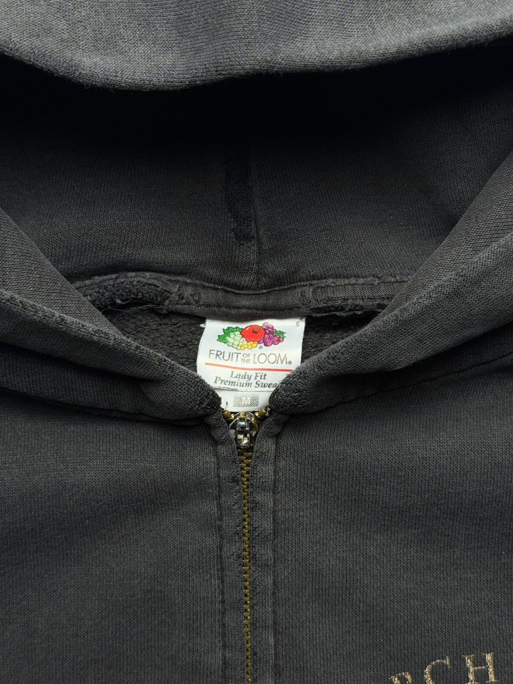 Makroaufnahme des Kragens und Reißverschlusses mit dem originalen weißen Nackenetikett der Marke „Fruit of the Loom Lady Fit Premium Sweat“ (Größe M).