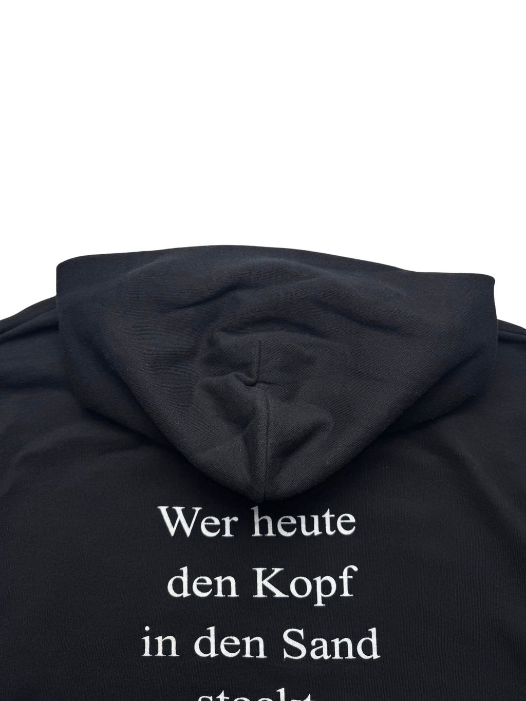 Detailansicht der Kapuze von hinten auf dem schwarzen Baumwoll-Sweatshirt-Stoff oberhalb des Rückendrucks.