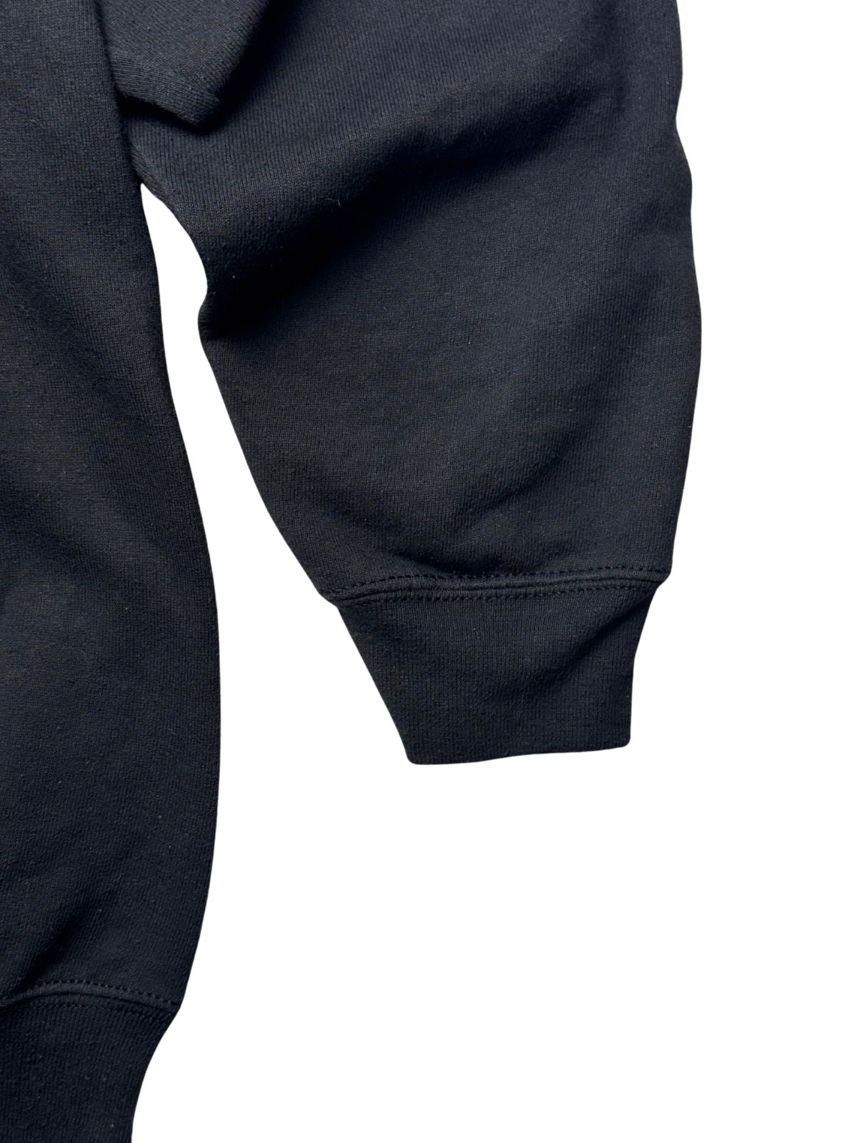 Detailansicht des Ärmels mit geripptem Bündchen auf dichtem schwarzen Sweatshirt-Material.