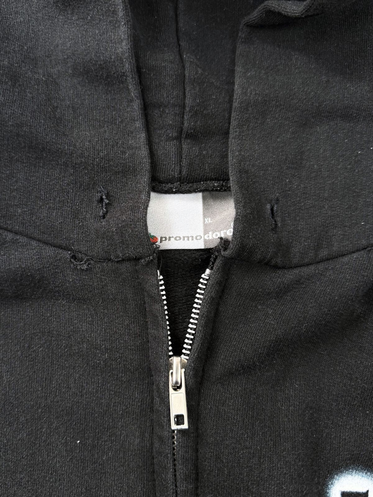 Nahaufnahme des Kragenbereichs am Die Ärzte Zip-Hoodie; zeigt deutliche Gebrauchsspuren in Form von kleinen Löchern und ausgefransten Stellen am Kapuzenansatz sowie das Promodoro-Tag.