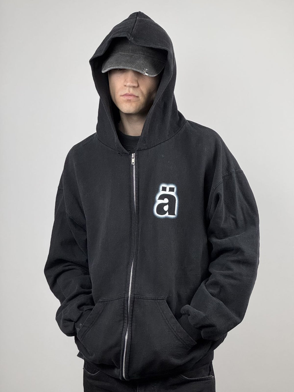 Ein Model trägt den schwarzen Vintage Die Ärzte Hoodie von 1998 mit tief gezogener Kapuze und Cap; zeigt den markanten Kontrast des „ä“-Logos und den authentischen Distressed-Look.
