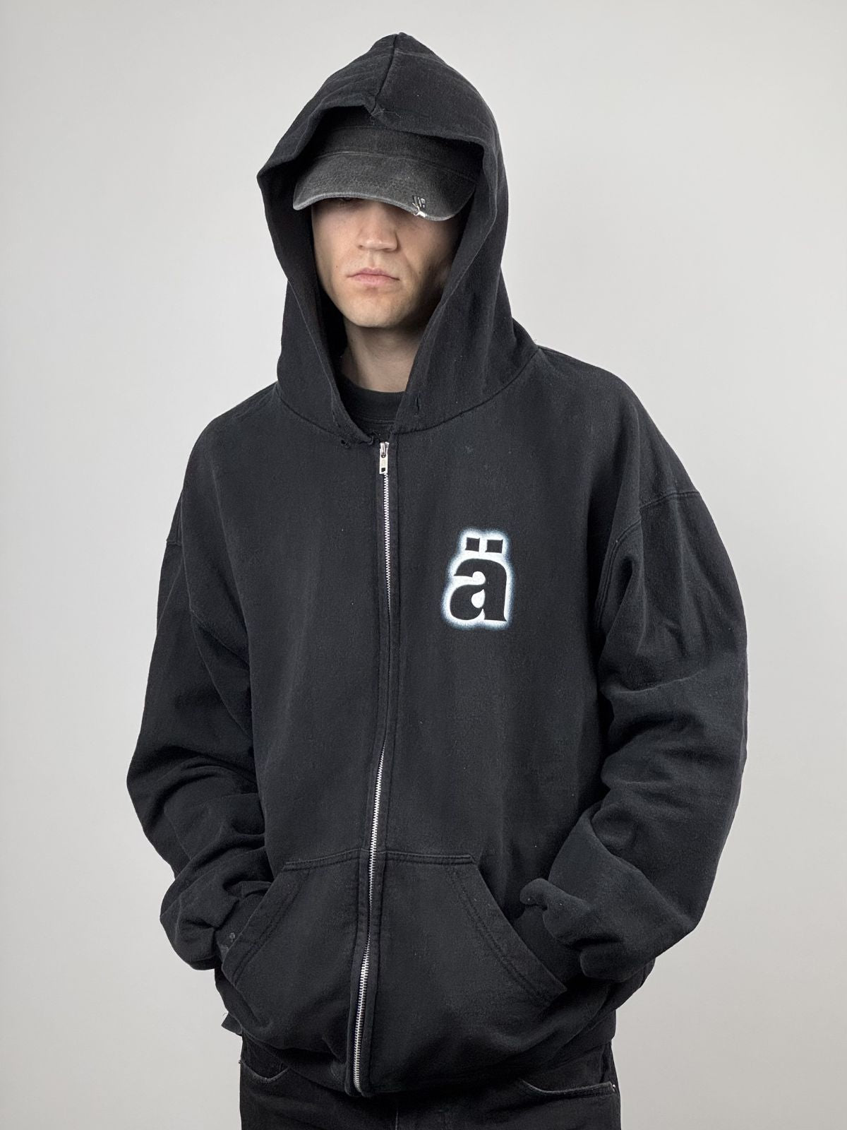 Ein Model trägt den schwarzen Vintage Die Ärzte Hoodie von 1998 mit tief gezogener Kapuze und Cap; zeigt den markanten Kontrast des „ä“-Logos und den authentischen Distressed-Look.
