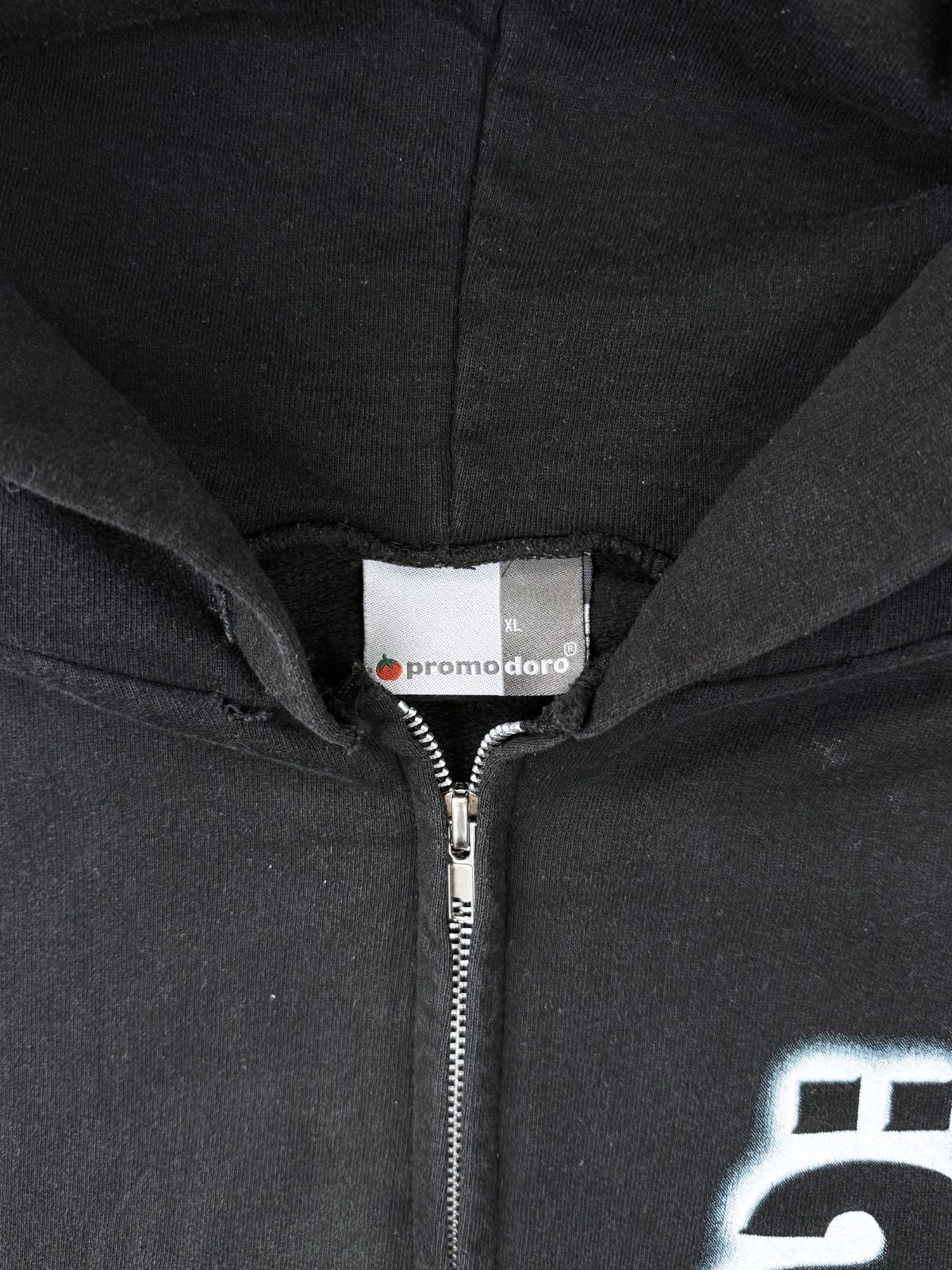 Nahaufnahme des Nackenetiketts: Weißes „Promodoro“ Tag mit rotem Tomaten-Logo, Größe XL, am Reißverschluss des Hoodies.