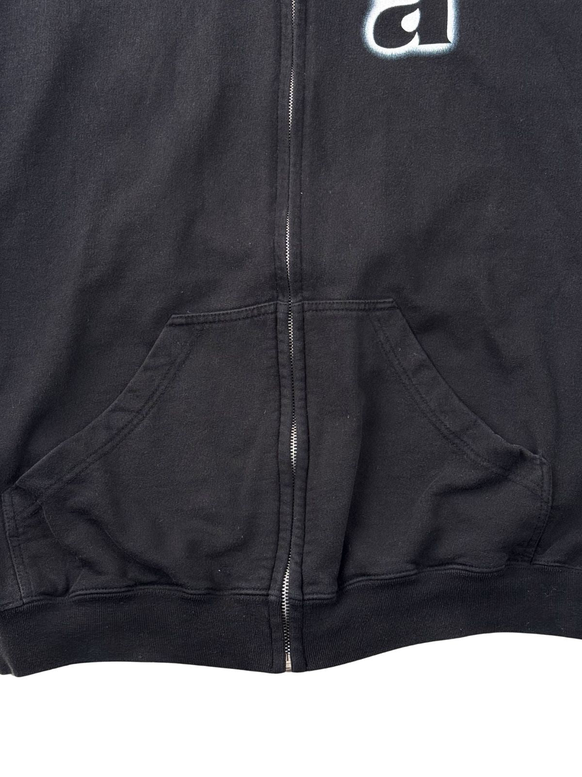 Fokus auf den silbernen Metall-Reißverschluss und die Kängurutaschen im unteren Bereich des schwarzen Band-Hoodies.