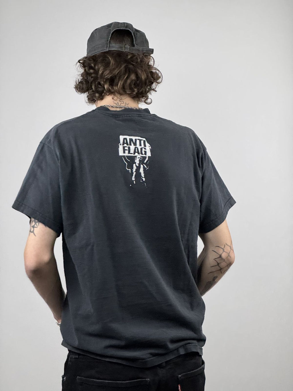 Rückansicht des getragenen Anti-Flag Shirts kombiniert mit einer schwarzen Cap; verdeutlicht die Platzierung des Logos im oberen Rückenbereich.