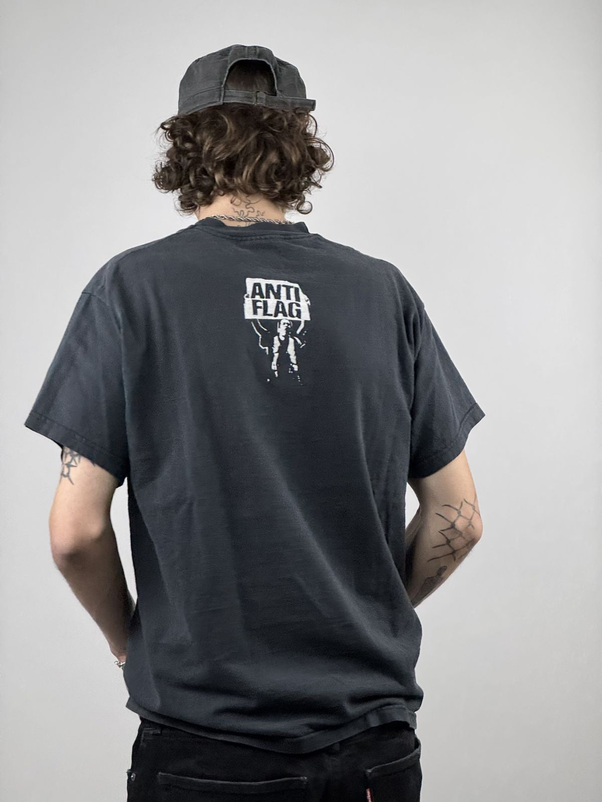 Rückansicht des getragenen Anti-Flag Shirts kombiniert mit einer schwarzen Cap; verdeutlicht die Platzierung des Logos im oberen Rückenbereich.