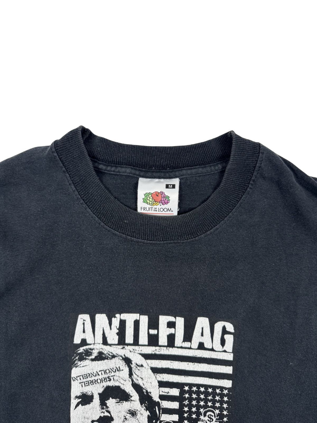 Nahaufnahme des Nackenbereichs mit einem weißen „Fruit of the Loom“ Etikett, Größe M, auf dem schwarzen Punk-Rock-Shirt.