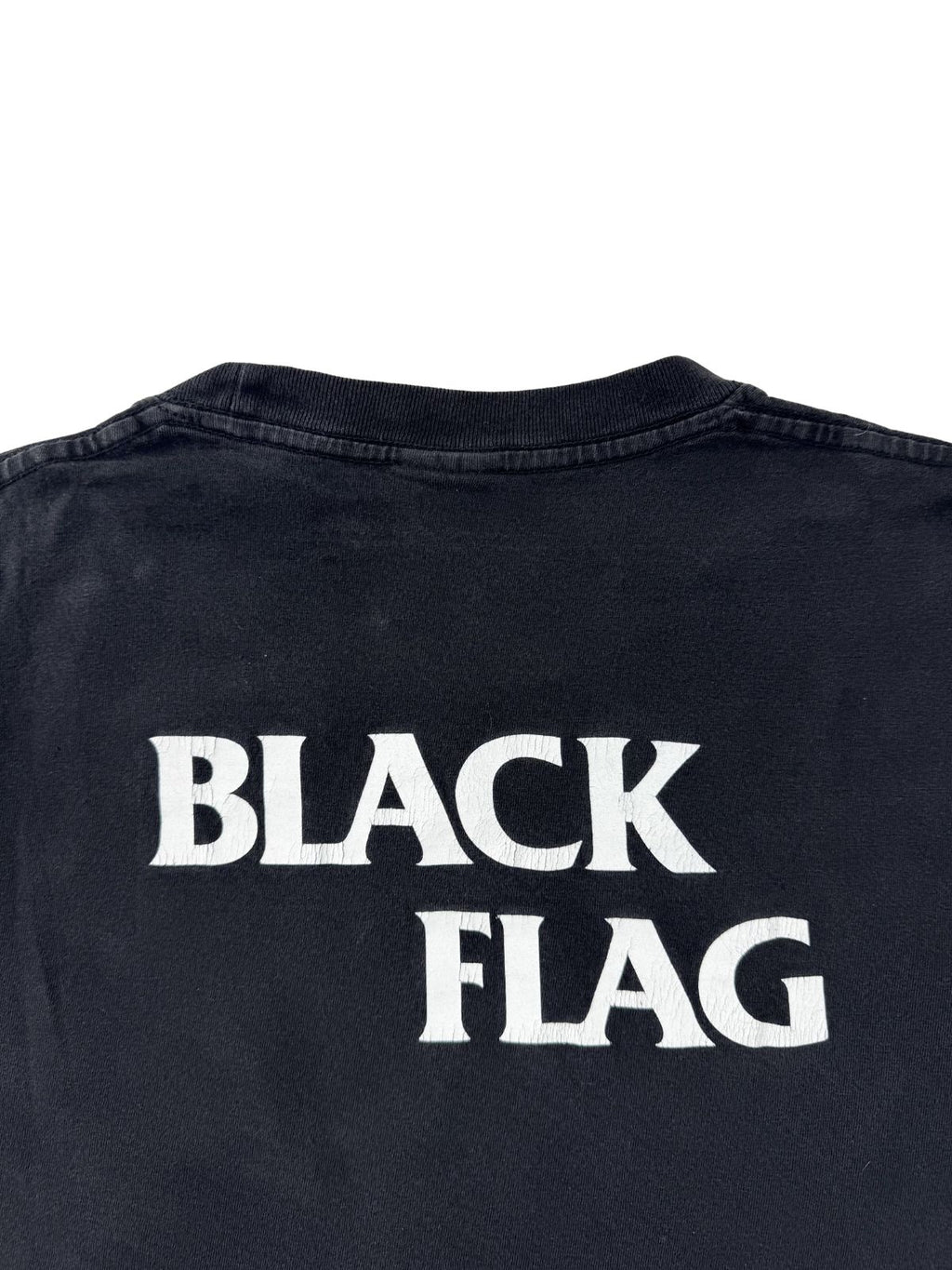 Rückansicht des verwaschenen schwarzen T-Shirts; zeigt einen schlichten, weißen "BLACK FLAG" Schriftzug mittig im Nackenbereich.
