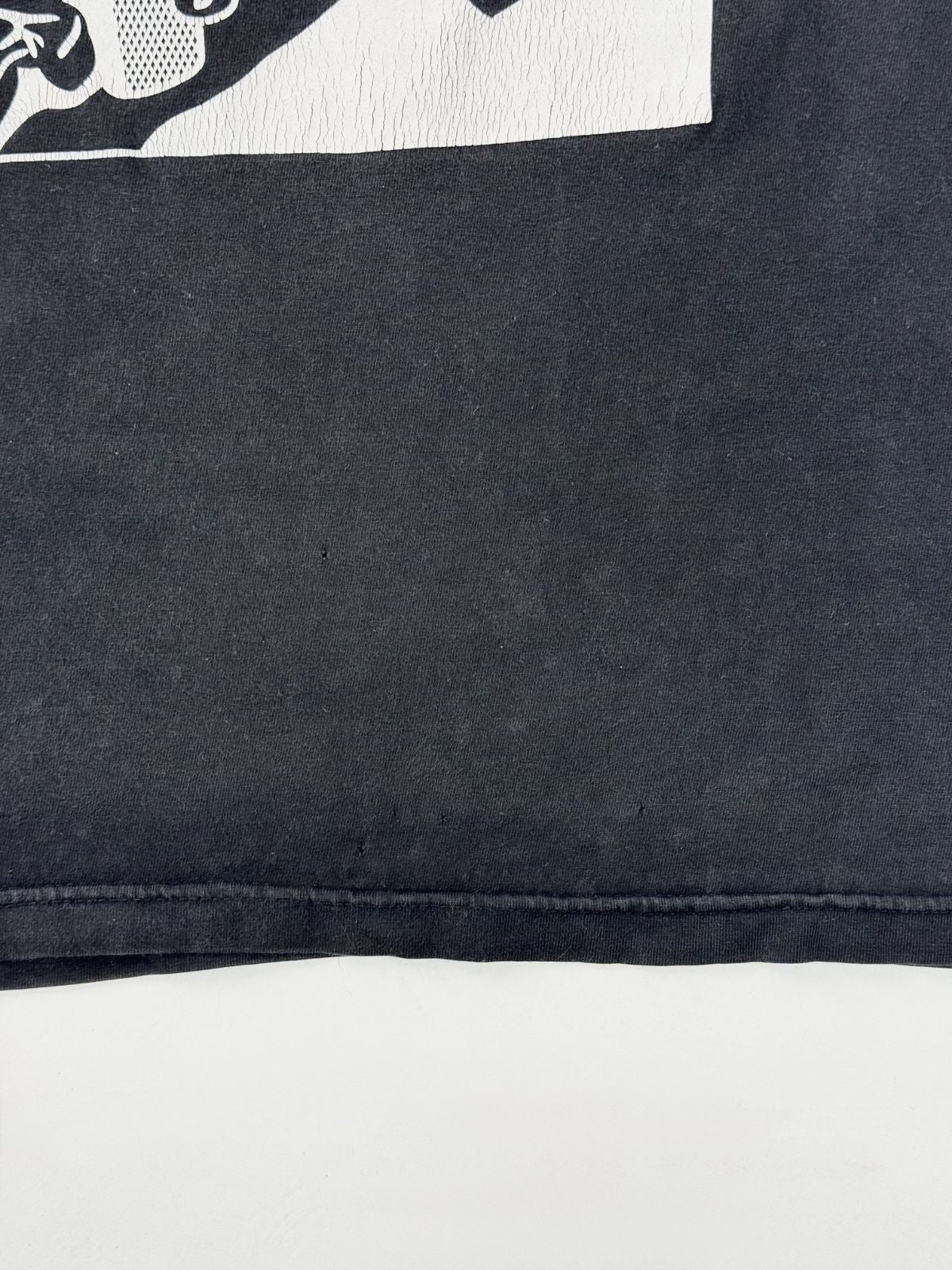 Transparente Nahaufnahme eines kleinen Lochs (Pin-Hole) im schwarzen Baumwollstoff – typisches Merkmal für authentische Vintage-Kleidung.