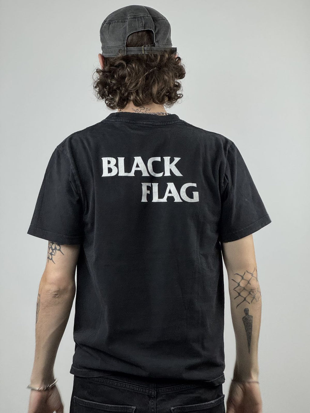 Rückansicht des getragenen Black Flag Shirts kombiniert mit einer schwarzen Mütze; verdeutlicht die Platzierung des Backprints.