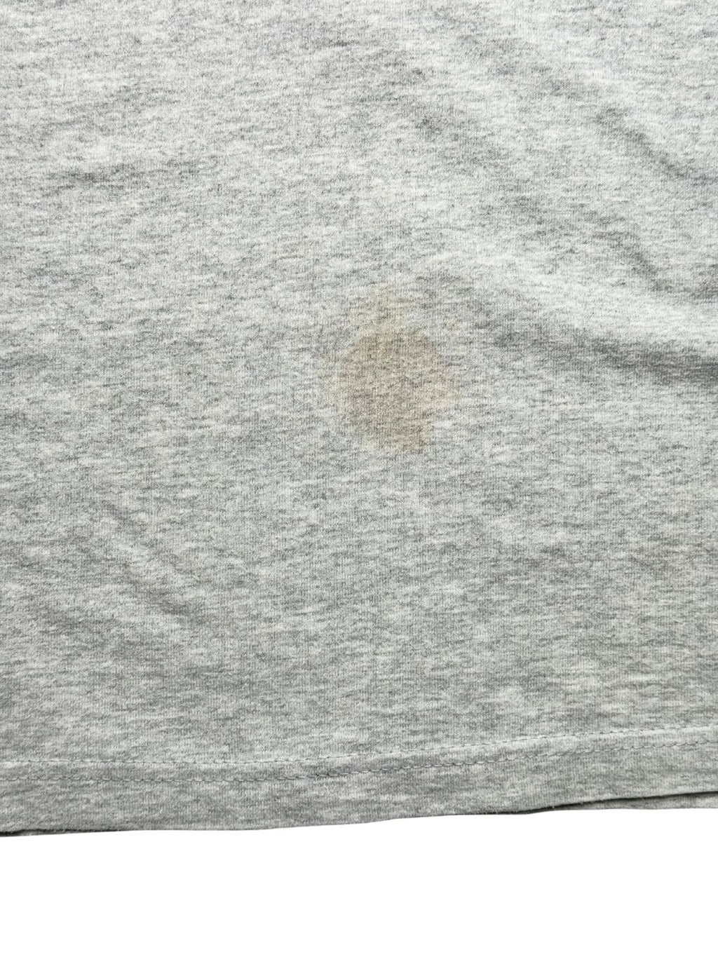 Detailaufnahme der unteren Vorderseite mit einem deutlich sichtbaren, kreisrunden Flecken (Stain) auf dem grauen Baumwollmaterial.