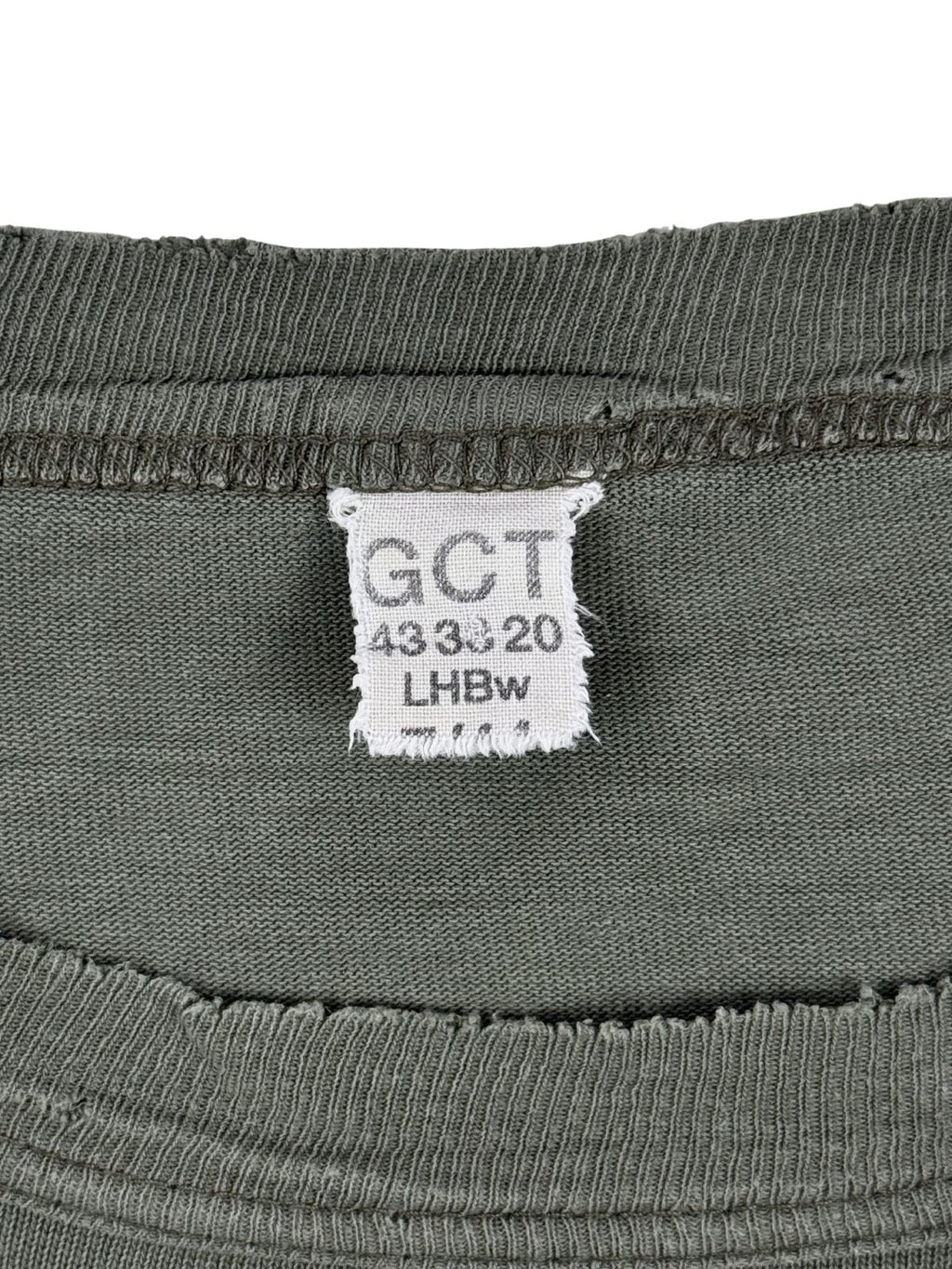 Nahaufnahme des originalen weißen Textiletiketts im Kragen des Vintage Bundeswehr-Shirts. Zu sehen sind die typischen Militär-Prägungen „GCT“, die Größenkennzeichnung „43 33 20“ und das Kürzel der offiziellen Bekleidungsgesellschaft „LHBw“. Ein unverzichtbares Authentizitätsmerkmal für Sammler.