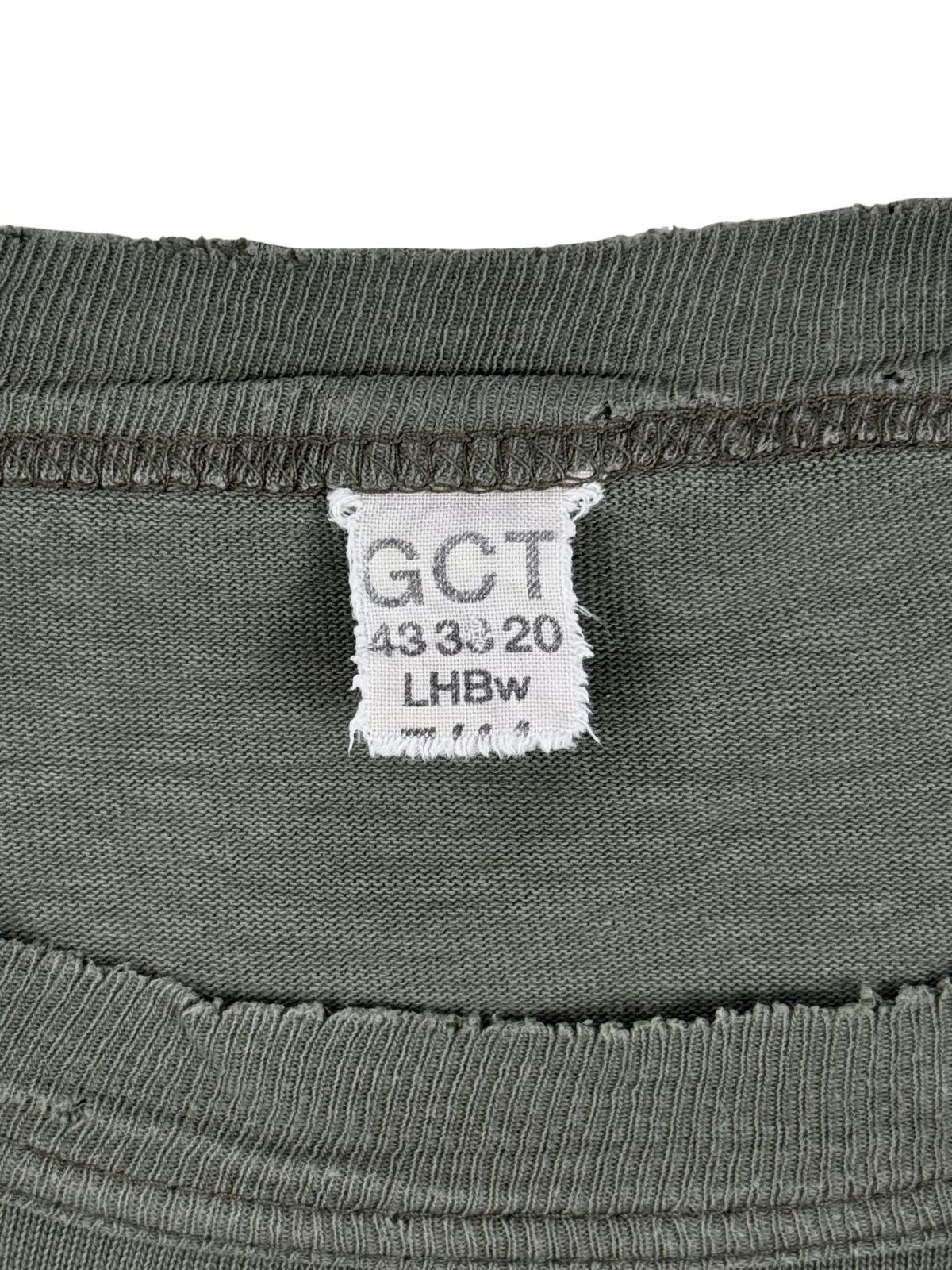 Nahaufnahme des originalen weißen Textiletiketts im Kragen des Vintage Bundeswehr-Shirts. Zu sehen sind die typischen Militär-Prägungen „GCT“, die Größenkennzeichnung „43 33 20“ und das Kürzel der offiziellen Bekleidungsgesellschaft „LHBw“. Ein unverzichtbares Authentizitätsmerkmal für Sammler.
