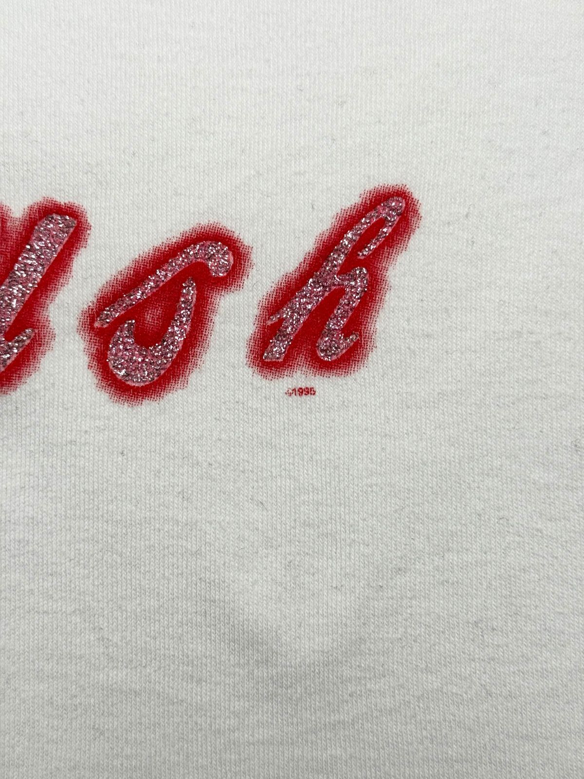 Makroaufnahme des Glitzer-Siebdrucks mit der sichtbaren Copyright-Zeile „©1995“ unter dem Buchstaben „h“ des Band-Logos.