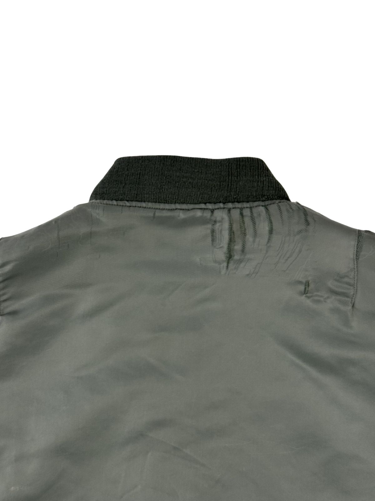 Detailaufnahme der oberen Rückseite knapp unterhalb des Kragenbündchens. Das graue Nylon-Gewebe zeigt deutliche Tragespuren mit gerafften, gezogenen Fäden und kleineren Materialfehlern auf der rechten Seite.