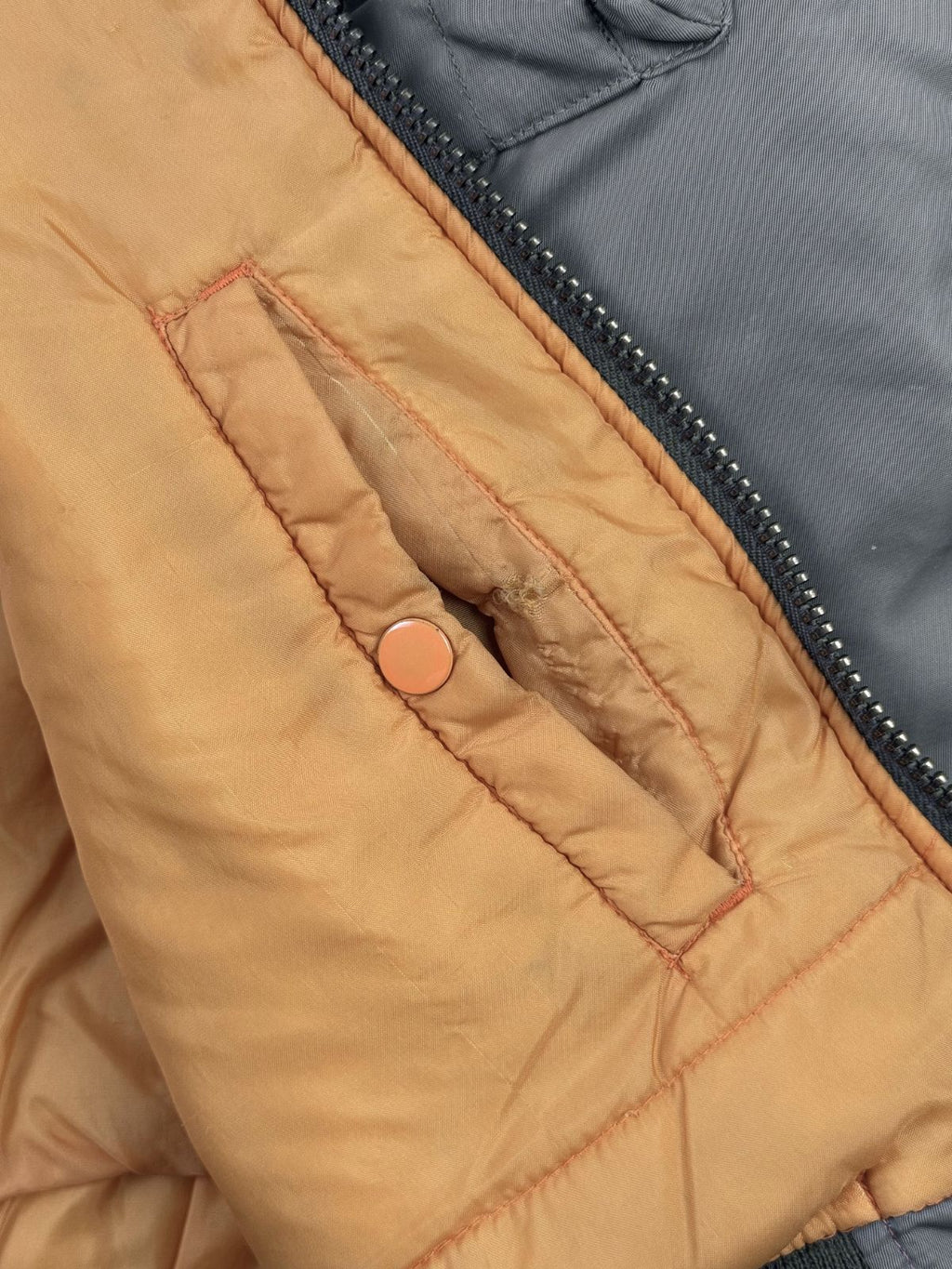 Detailansicht der linken Innentasche im orangefarbenen Futter. Am oberen Rand des Eingriffs, direkt über dem Druckknopf, ist der Stoff an der Naht leicht eingerissen und ausgefranst.