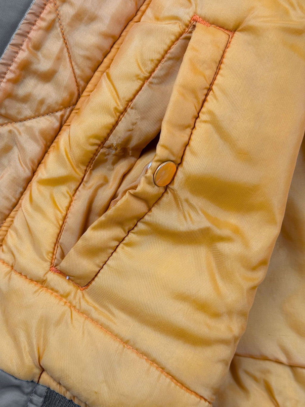 Detailaufnahme der rechten Innentasche im orangenen Nylon-Futter mit einem kleinen Loch oder Riss im Stoffgewebe direkt neben dem kupferfarbenen Druckknopf.