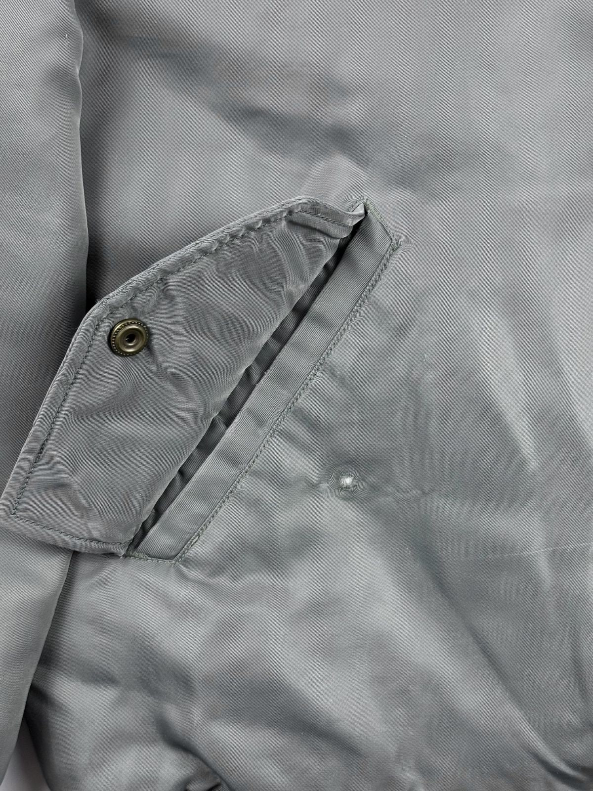 Detailaufnahme der rechten Seitentasche zur Mängelüberprüfung. Der graue Stoff weist knapp unterhalb der Taschenöffnung eine kleine, kreisrunde Beschädigung (mögliches Brandloch oder Abrieb) auf.