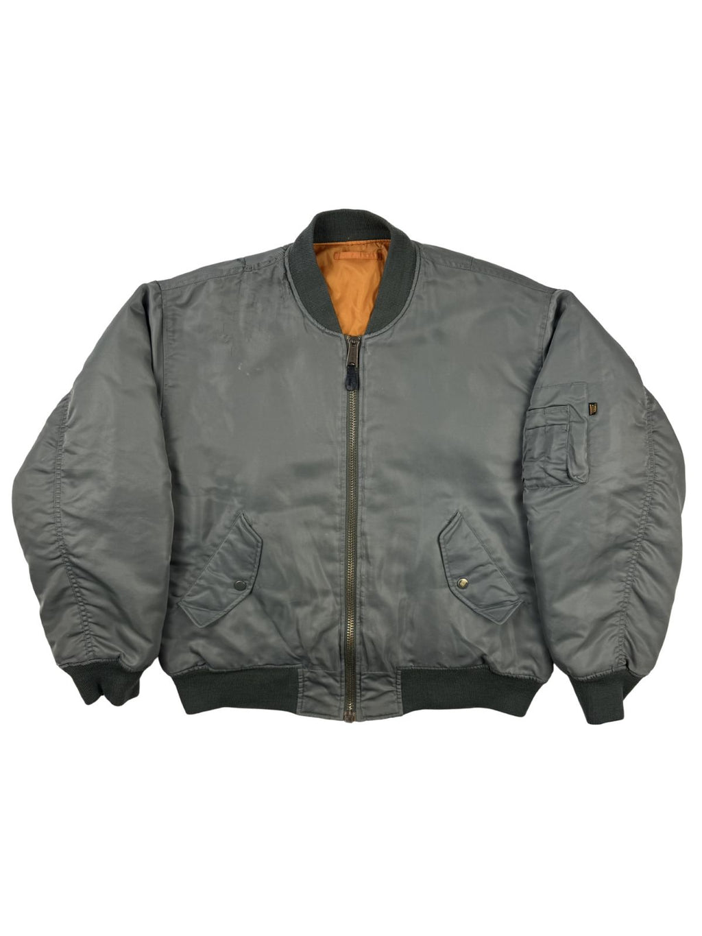 Komplettansicht der Vorderseite einer grauen Vintage MA-1 Bomberjacke der Marke Buster aus dem Jahr 1996. Die klassische Fliegerjacke (Flight Jacket) besitzt ein orangefarbenes Innenfutter, eine Ärmeltasche und zwei schräge Seitentaschen. Flatlay auf weißem Hintergrund.