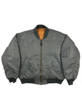 Komplettansicht der Vorderseite einer grauen Vintage MA-1 Bomberjacke der Marke Buster aus dem Jahr 1996. Die klassische Fliegerjacke (Flight Jacket) besitzt ein orangefarbenes Innenfutter, eine Ärmeltasche und zwei schräge Seitentaschen. Flatlay auf weißem Hintergrund.
