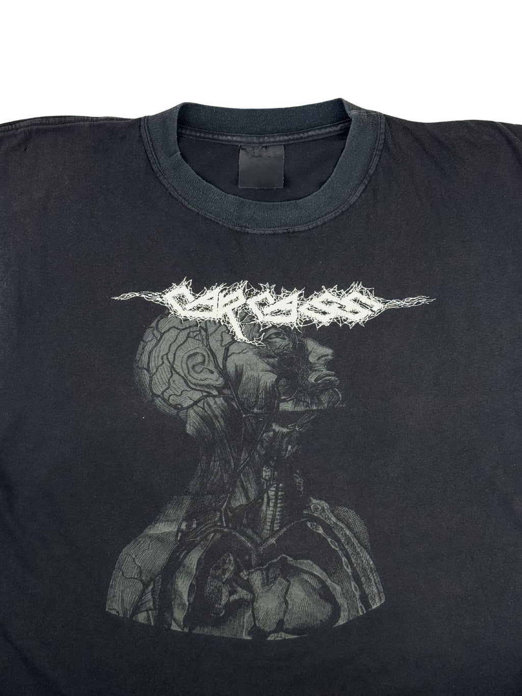 Detailansicht der Vorderseite des Carcass Shirts mit Fokus auf den Rundhalsausschnitt und das detaillierte Artwork des medizinischen Kopfschnitts unter dem gezackten Bandlogo.