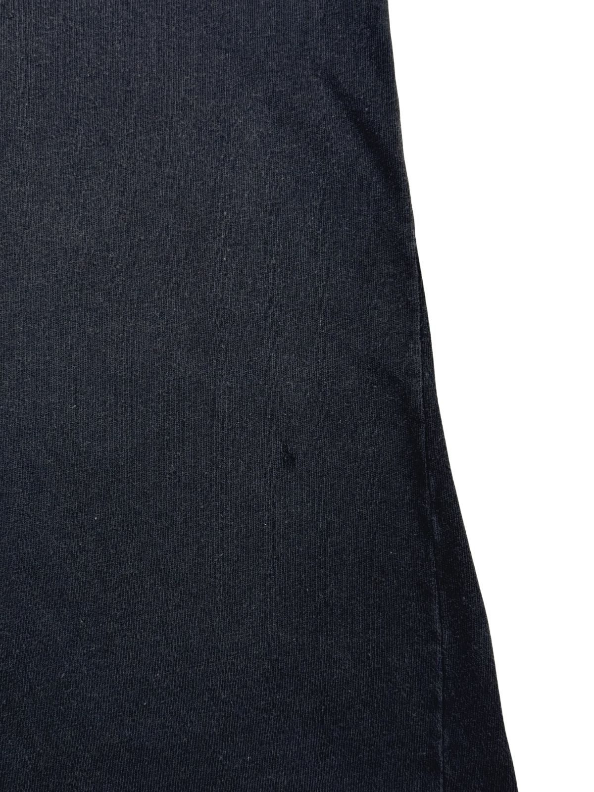 Detailaufnahme der Stoffoberfläche mit einem kleinen, authentischen Loch (Pinhole) im schwarzen Baumwollmaterial.