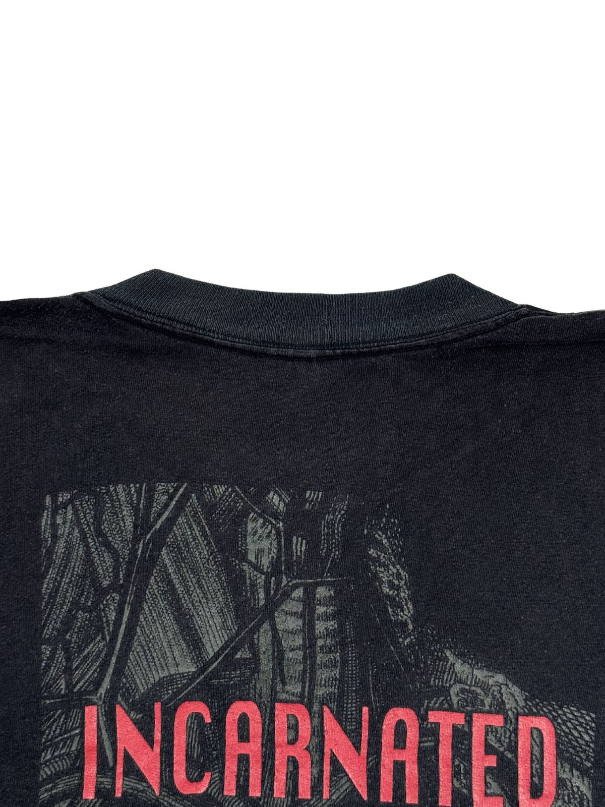 Detailaufnahme der oberen Rückseite des Shirts mit dem gerippten Halsbündchen und dem Beginn des roten „INCARNATED...“-Schriftzugs auf der verdunkelten Grafik.