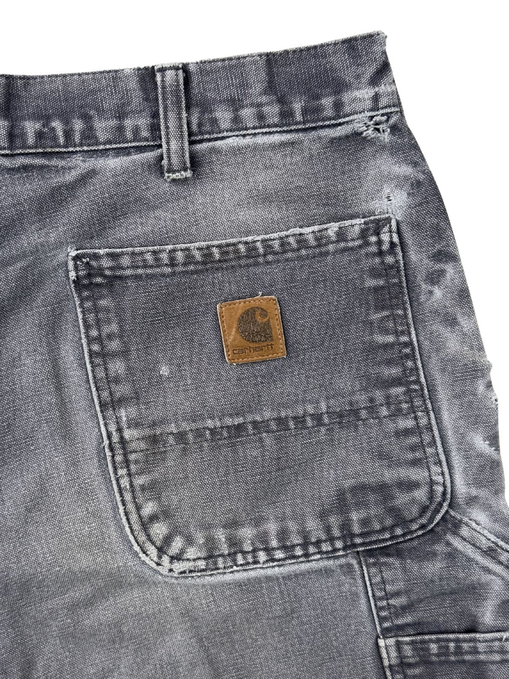 Detail der Gesäßtasche einer Carhartt Shorts mit dem quadratischen Leder-Logo-Patch und authentischer Abnutzung.