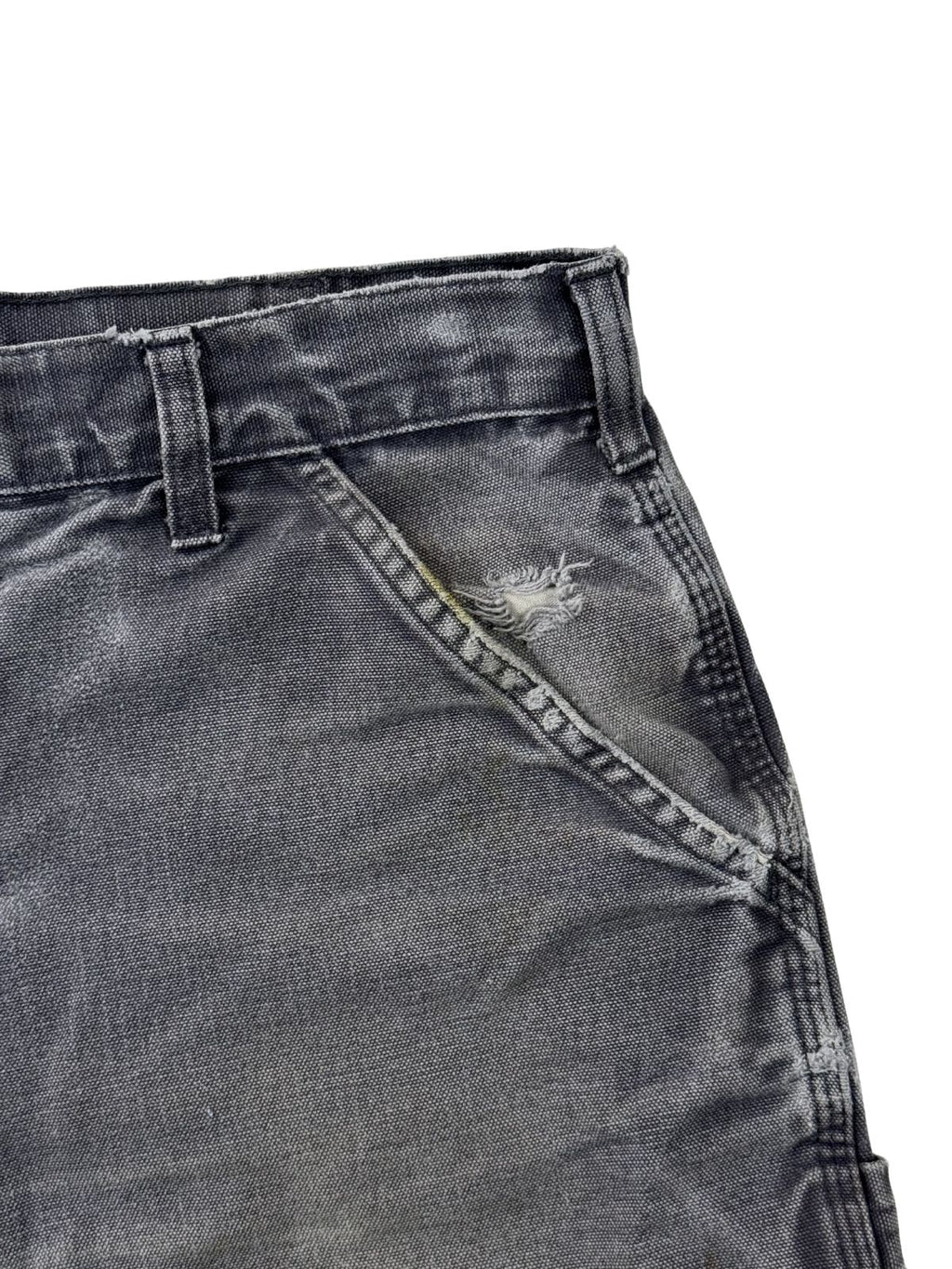 Detailansicht einer vorderen Tasche mit einem Loch und Distressed-Workwear-Look einer grauen Carhartt Shorts.