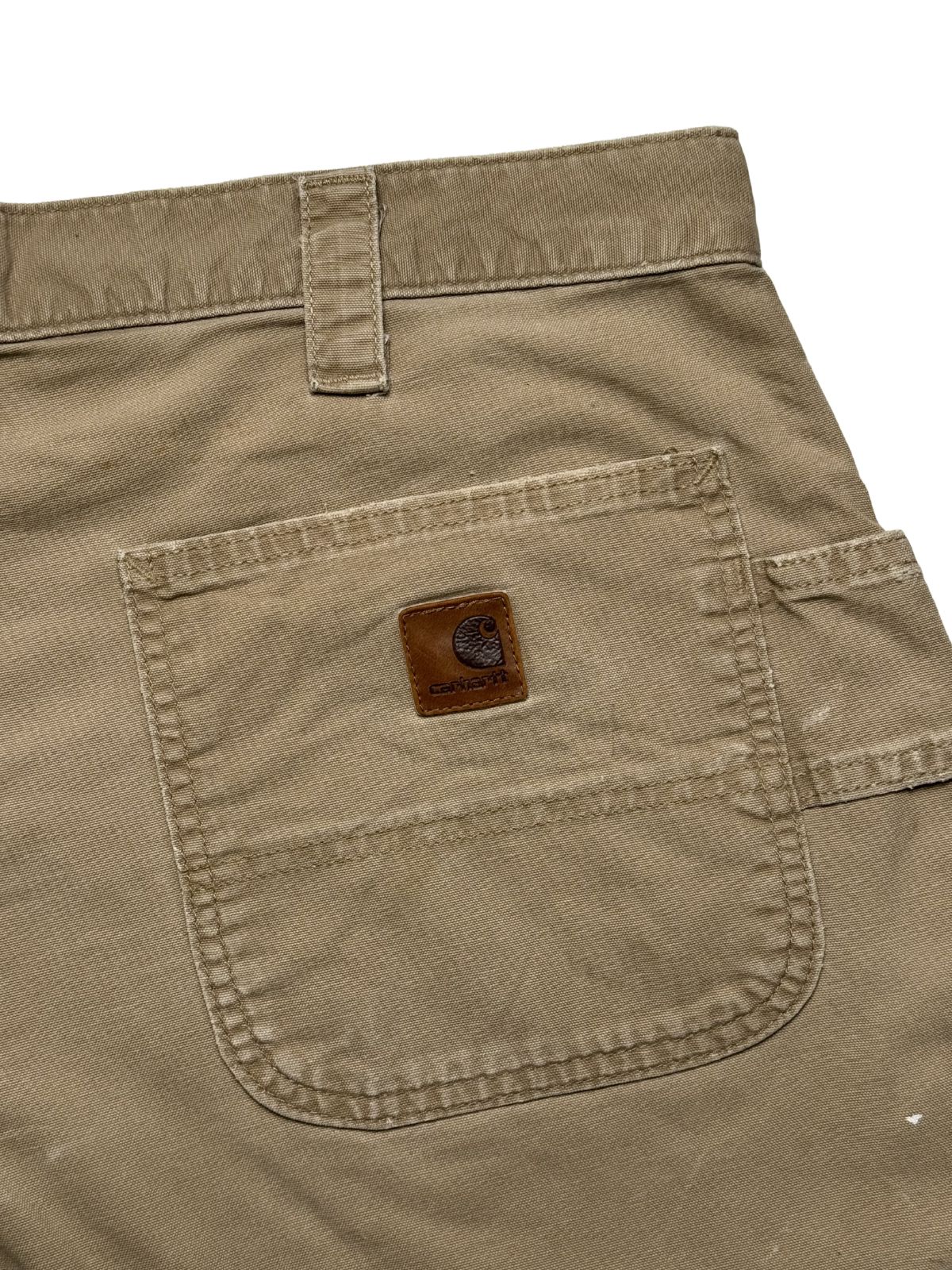 Detailaufnahme der hinteren rechten Gesäßtasche mit dem originalen, quadratischen Carhartt Logo-Patch aus braunem Leder.