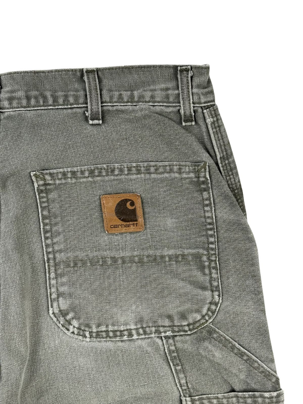 Nahaufnahme der rechten Gesäßtasche mit dem klassischen, quadratischen Carhartt-Logo-Patch aus Leder auf dem ausgewaschenen, grauen Duck-Canvas-Stoff.