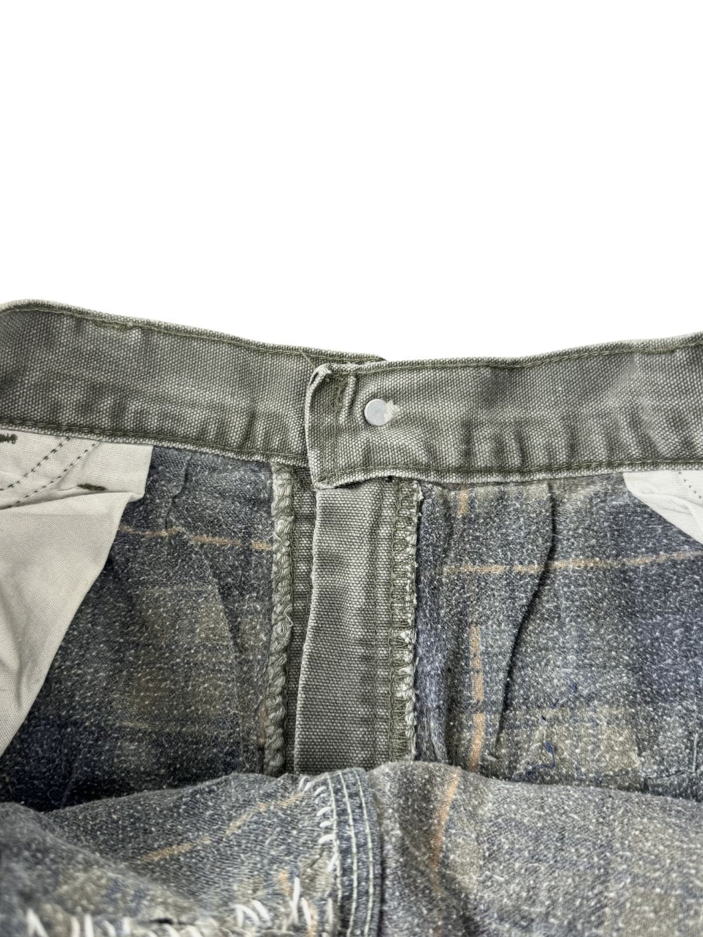 Detailansicht der geöffneten Bund-Innenseite. Zu sehen sind der metallene Hosenknopf, die robuste Webkante und das weiche, grau-blau karierte Flannel-Innenfutter (Flannel-Lining) für den Winter.