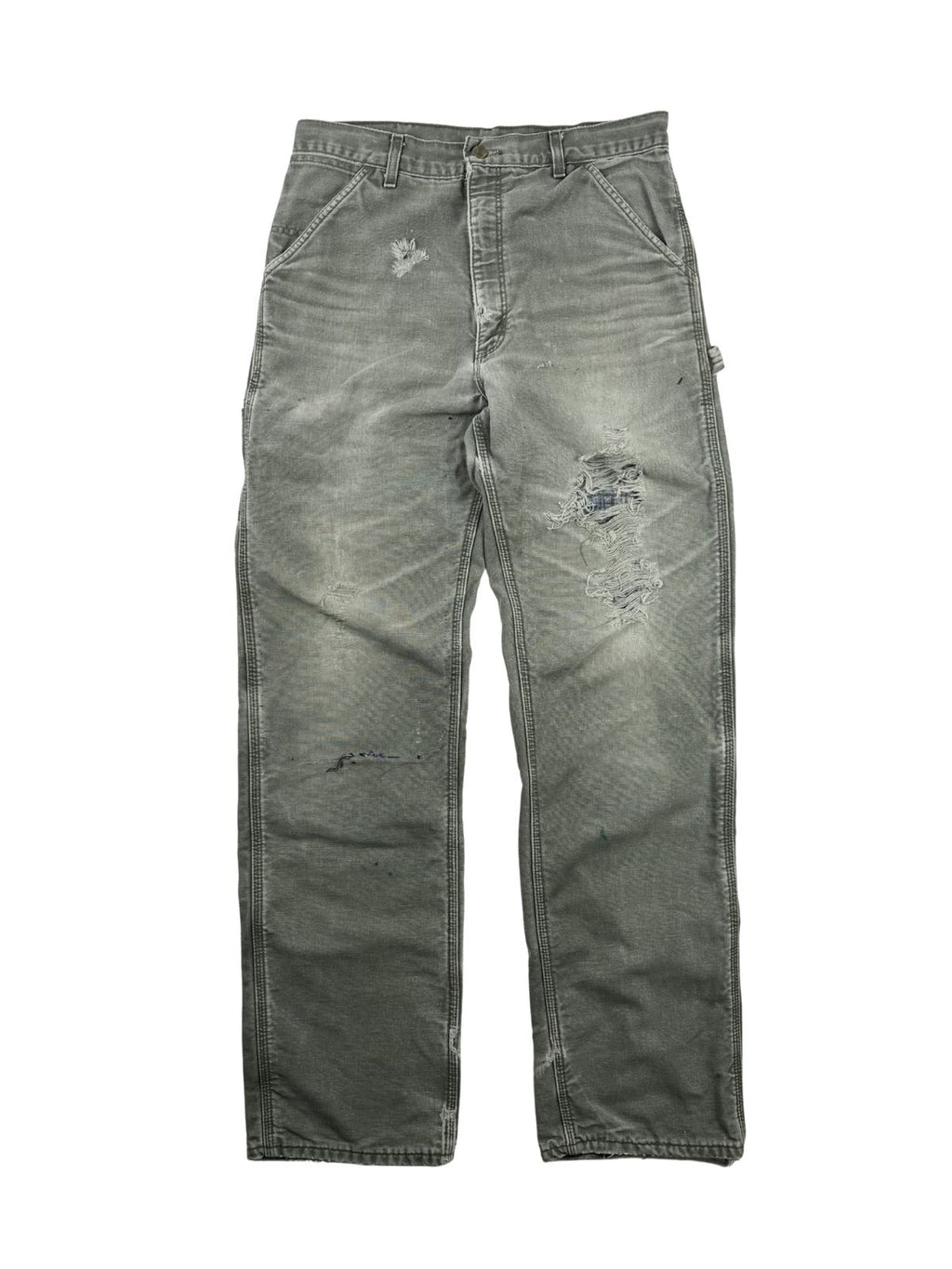 Komplettansicht der Vorderseite einer verwaschenen, grauen Vintage Carhartt Carpenter-Arbeitshose im Flatlay. Die gefütterte Workwear-Hose zeigt starken Distressed-Charakter mit einem kleinen Loch auf dem rechten Oberschenkel und einer großen Zerschleißung am linken Knie.