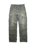 Komplettansicht der Vorderseite einer verwaschenen, grauen Vintage Carhartt Carpenter-Arbeitshose im Flatlay. Die gefütterte Workwear-Hose zeigt starken Distressed-Charakter mit einem kleinen Loch auf dem rechten Oberschenkel und einer großen Zerschleißung am linken Knie.