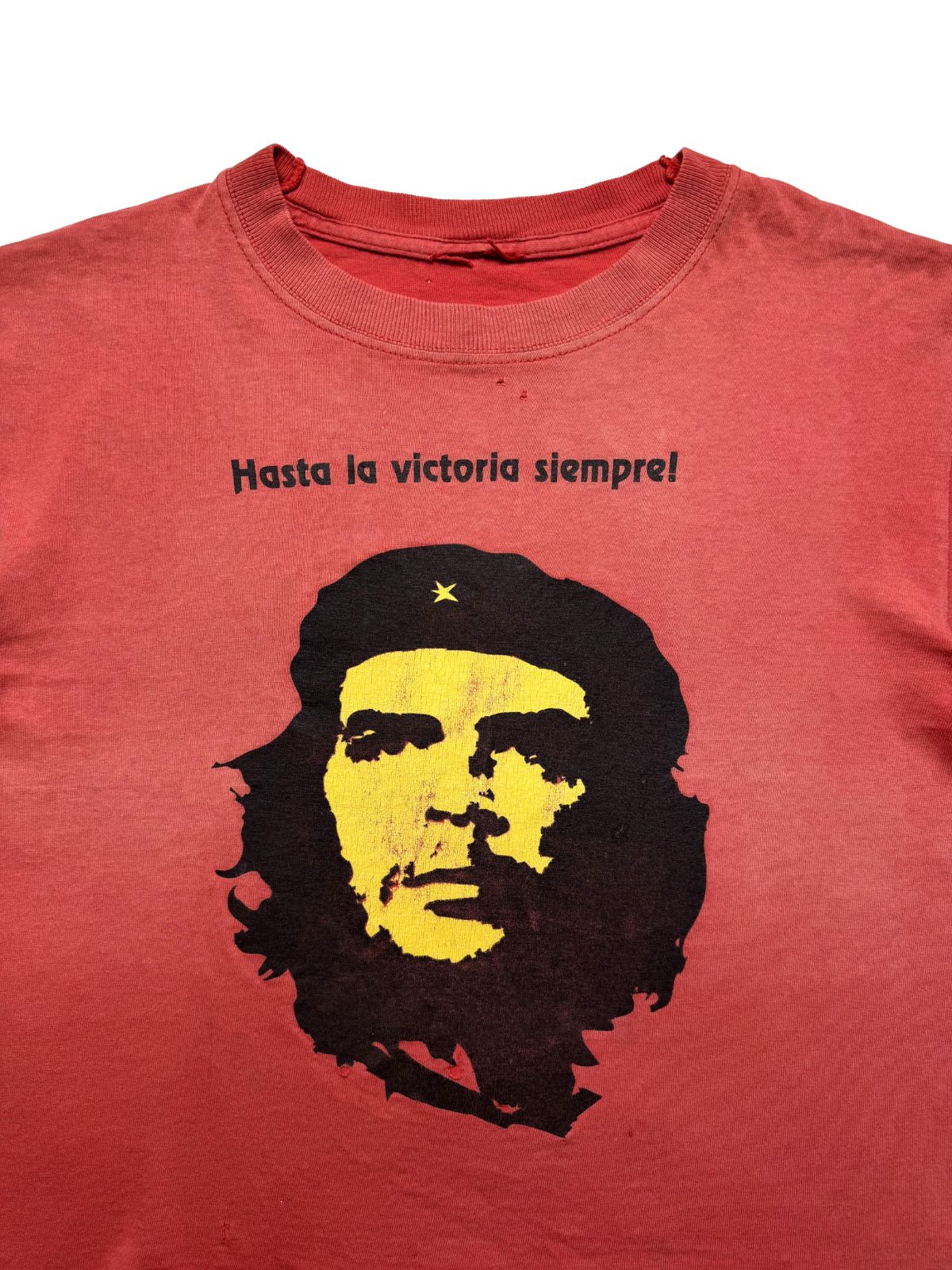 Nahaufnahme der oberen Frontpartie mit Blick auf den leicht gedehnten Rundhalsausschnitt, den Slogan-Print und zwei kleine Pins/Pinholes im roten Stoff.