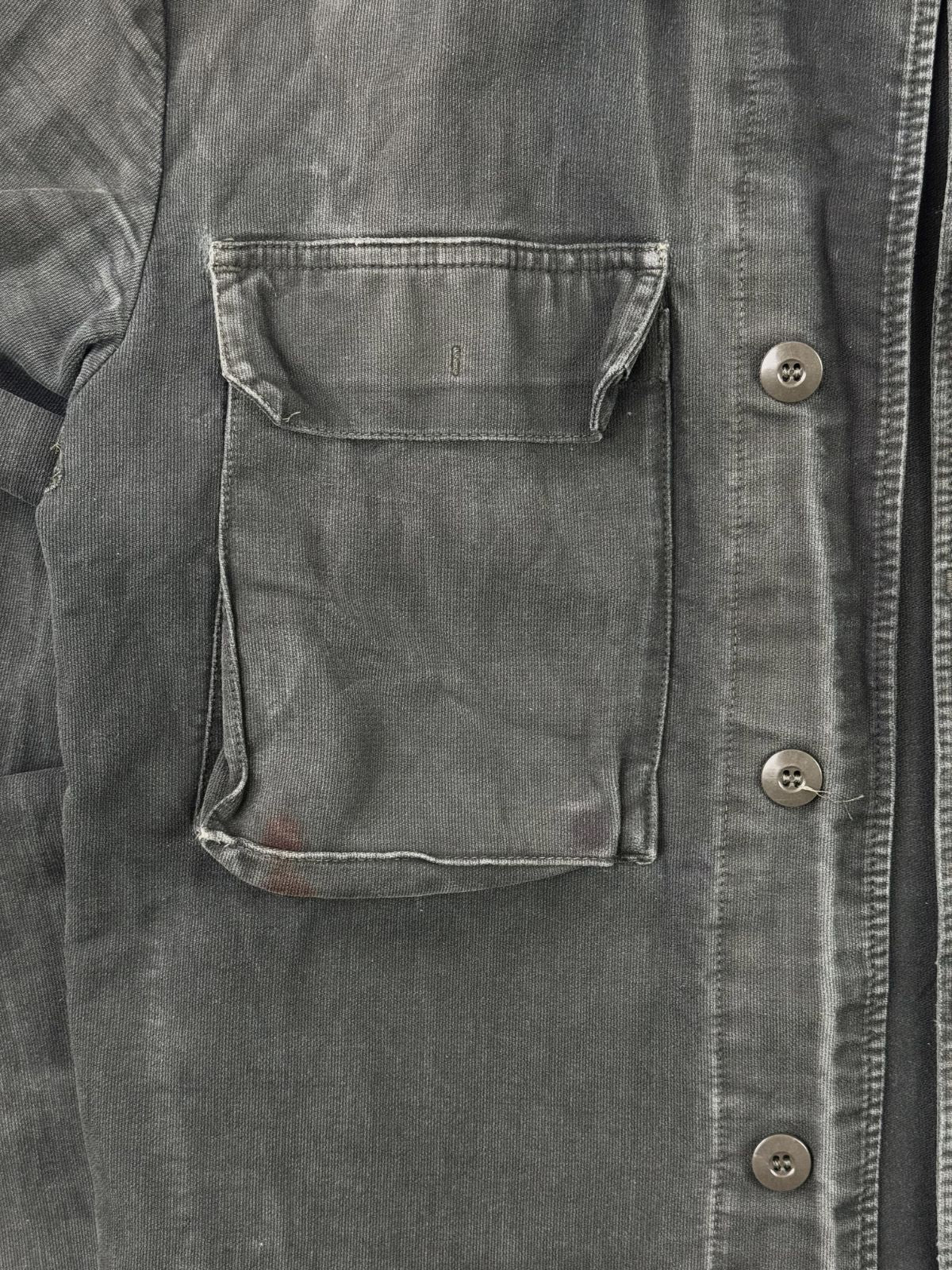 Detailaufnahme der rechten Brusttasche mit sichtbaren, rötlich-braunen Verfärbungen oder Flecken am unteren Rand der Tasche.