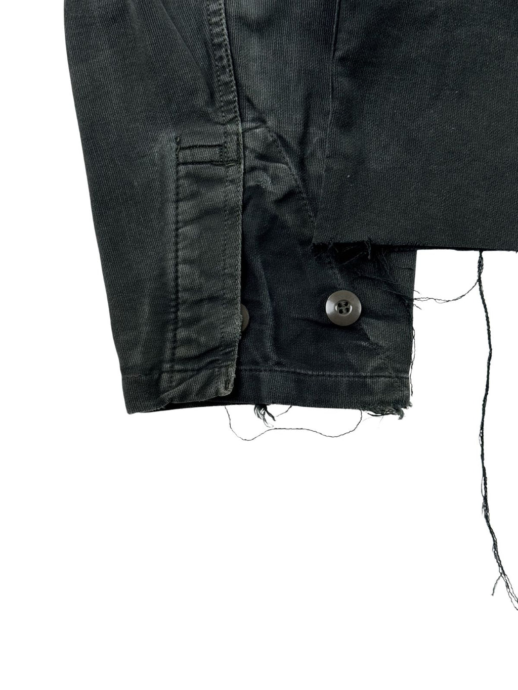 Detailaufnahme des linken Ärmelbündchens mit verstellbarem Knopfverschluss, die zudem die offene, ausgefranste Kante des kurzen Jackensaums zeigt.