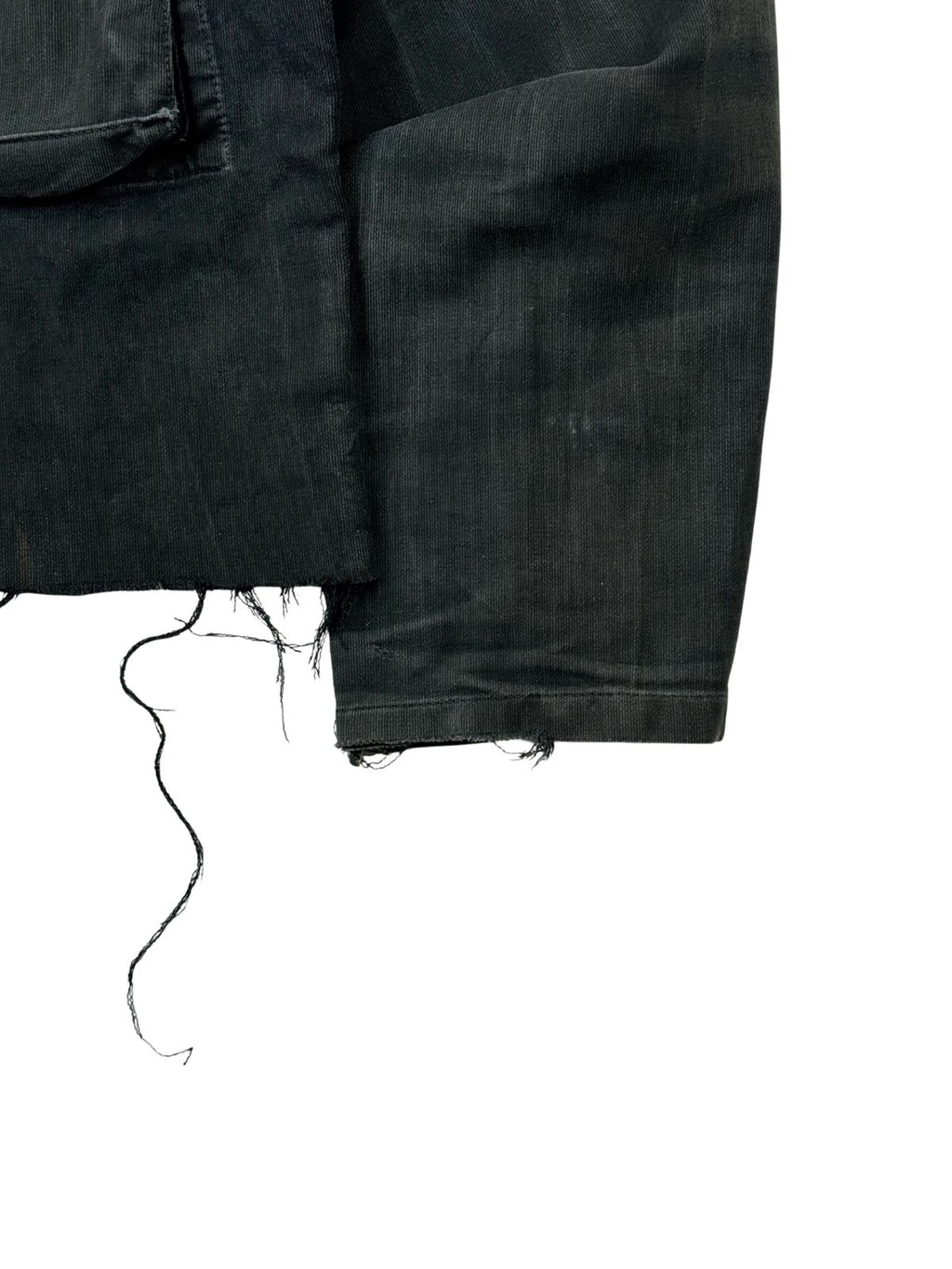 Detailansicht des linken Ärmelbündchens von der Vorderseite. Gut erkennbar sind die robusten Webstrukturen des schwarzen Moleskin-Stoffs sowie die herabhängenden Fäden des ungesäumten, abgeschnittenen Jackenrands direkt daneben.