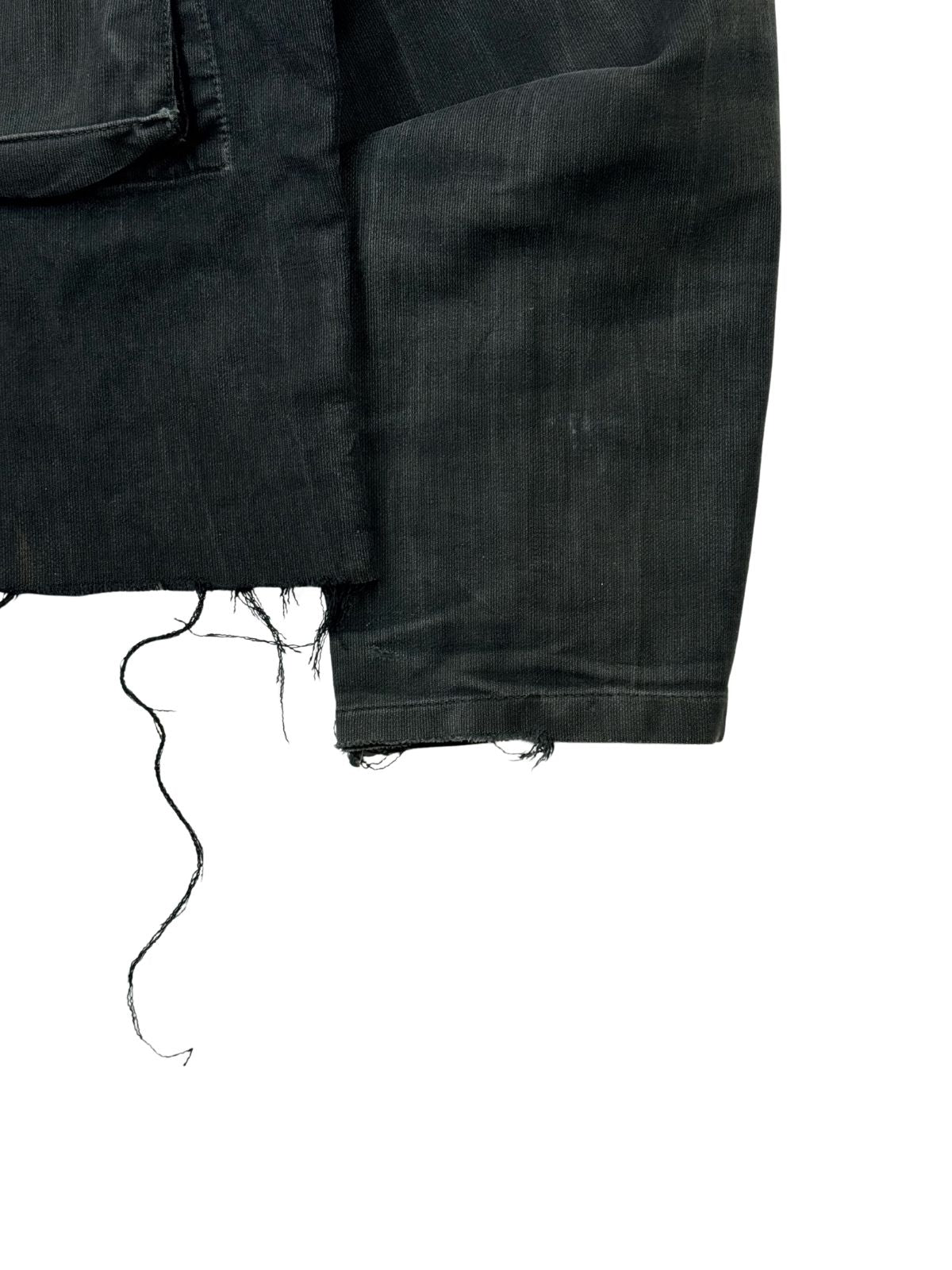 Detailansicht des linken Ärmelbündchens von der Vorderseite. Gut erkennbar sind die robusten Webstrukturen des schwarzen Moleskin-Stoffs sowie die herabhängenden Fäden des ungesäumten, abgeschnittenen Jackenrands direkt daneben.