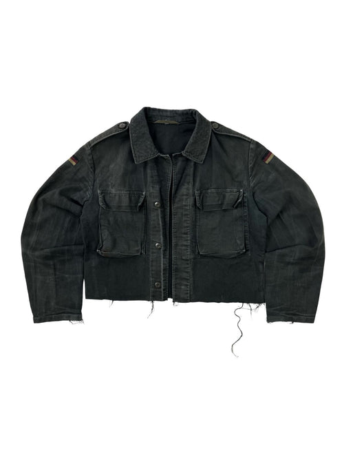 Komplettansicht der Vorderseite einer umgearbeiteten (cropped) Vintage Bundeswehr Feldjacke aus den 1980er Jahren in verwaschenem Schwarz. Die Moleskin-Jacke hat zwei große Brusttaschen, Schulterklappen, Flaggen-Patches auf den Ärmeln und einen kurz abgeschnittenen, ausgefransten Saum. Flatlay auf weißem Hintergrund.