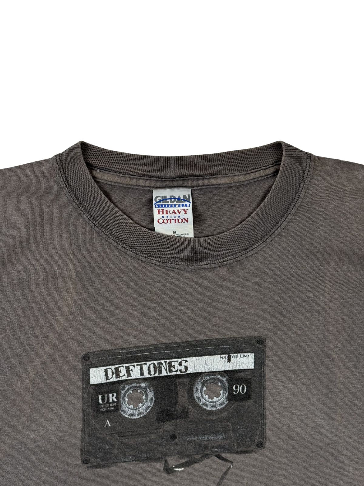 Detailansicht der Vorderseite des Deftones Shirts mit Fokus auf den Kassetten-Print (Tape) und das im Kragen sichtbare weiße „Gildan Heavy Cotton“-Etikett.