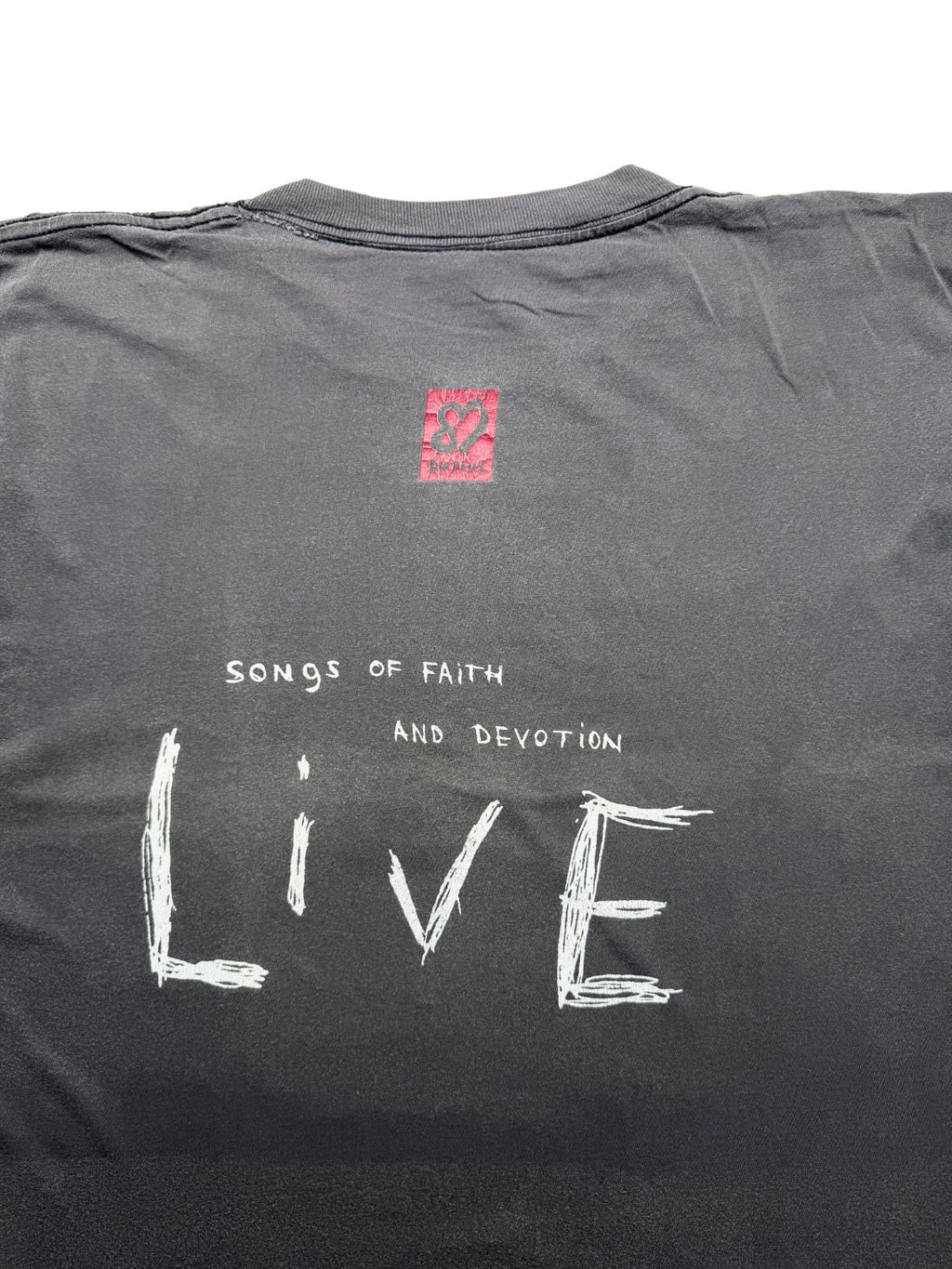 Nahaufnahme der oberen Rückseite mit Fokus auf den roten „DM“-Logo-Kasten und die weiße Aufschrift „Songs of Faith and Devotion LIVE“.