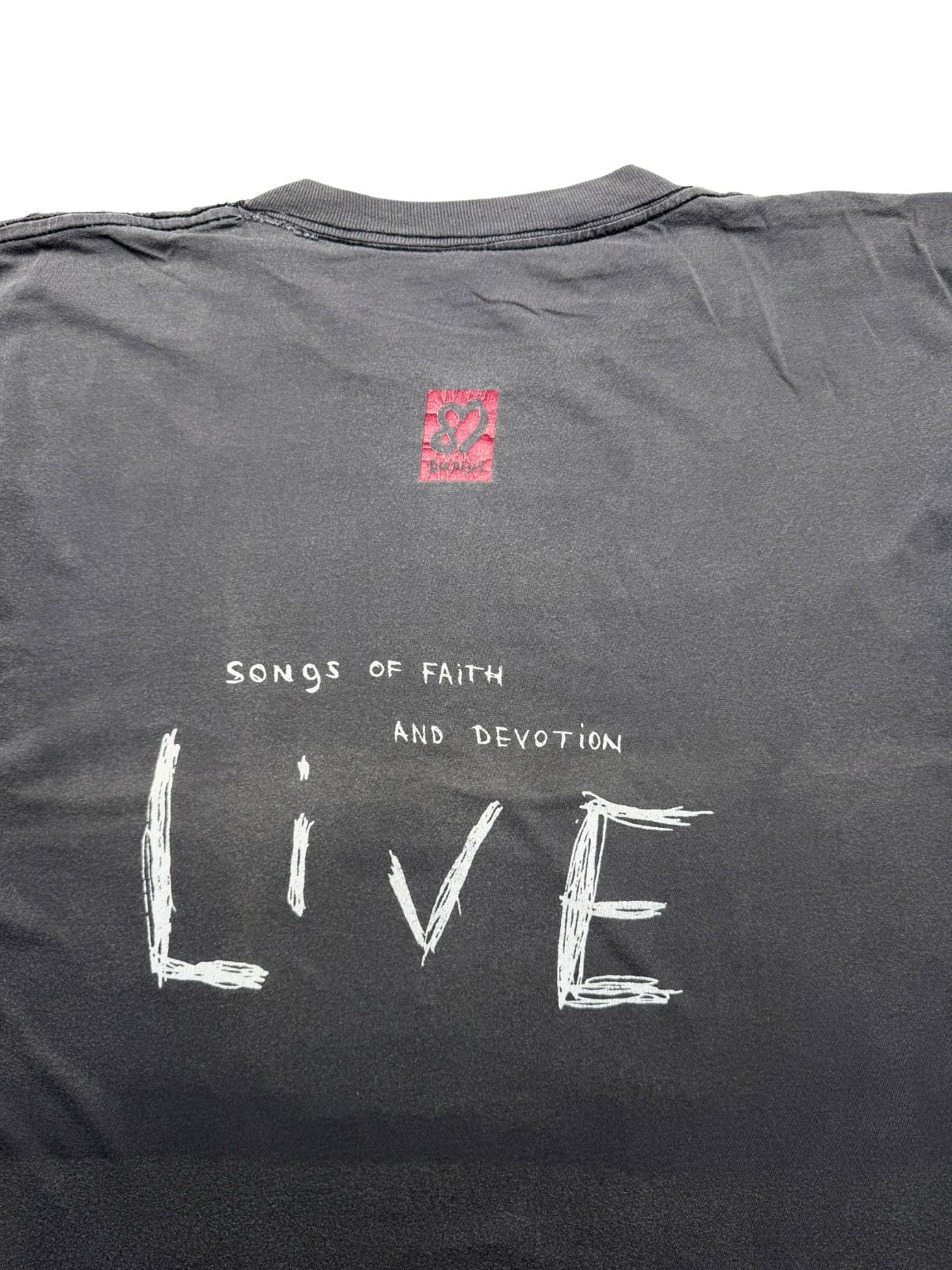 Nahaufnahme der oberen Rückseite mit Fokus auf den roten „DM“-Logo-Kasten und die weiße Aufschrift „Songs of Faith and Devotion LIVE“.