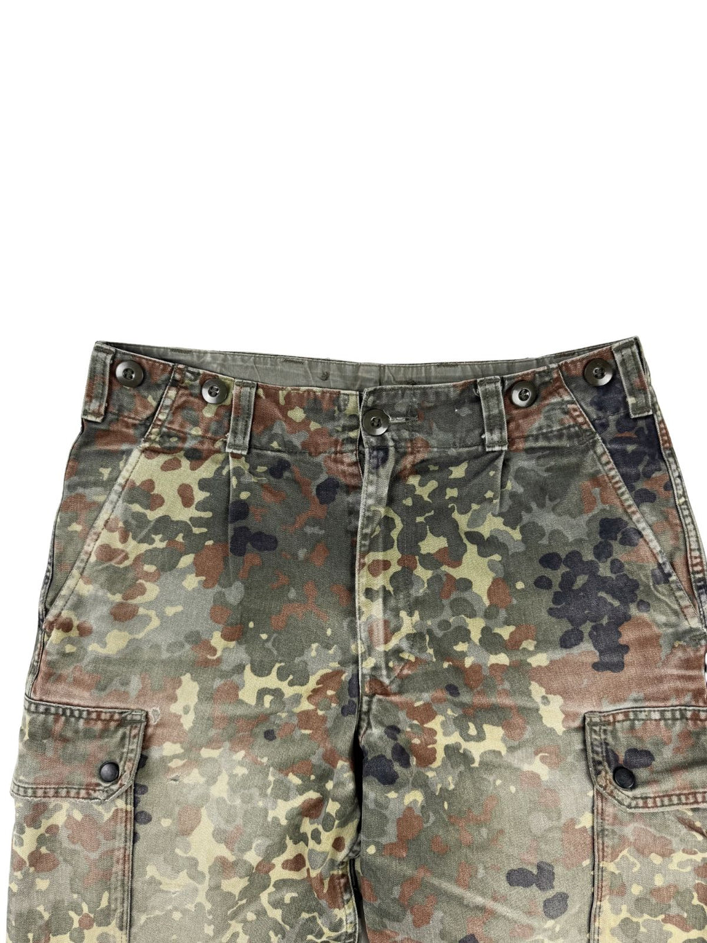 Detailansicht der vorderen Hüftpartie der Flecktarn-Hose. Gut erkennbar sind der Hosenbund mit Knöpfen für Hosenträger, Gürtelschlaufen, die Faltenlegung und die Ansätze der seitlichen Cargo-Taschen.